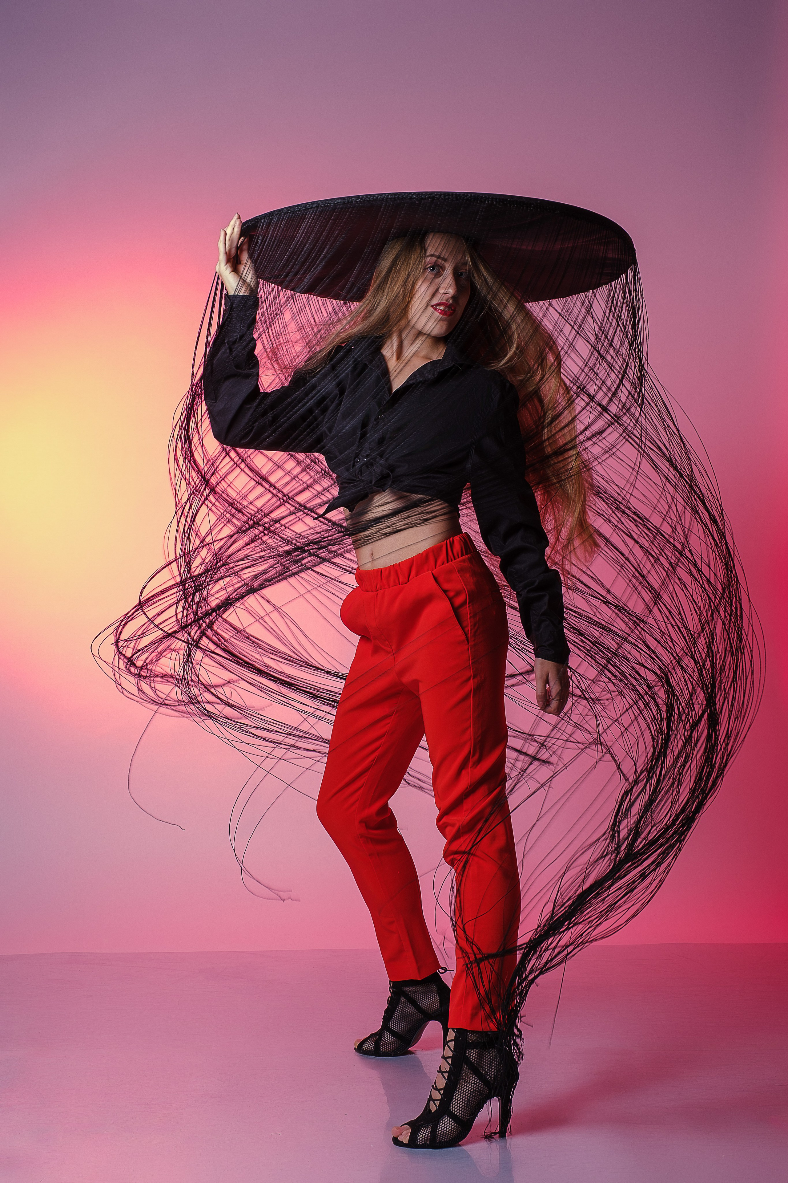 Девушка танцует в большой шляпе, с которой свисают нити до пола