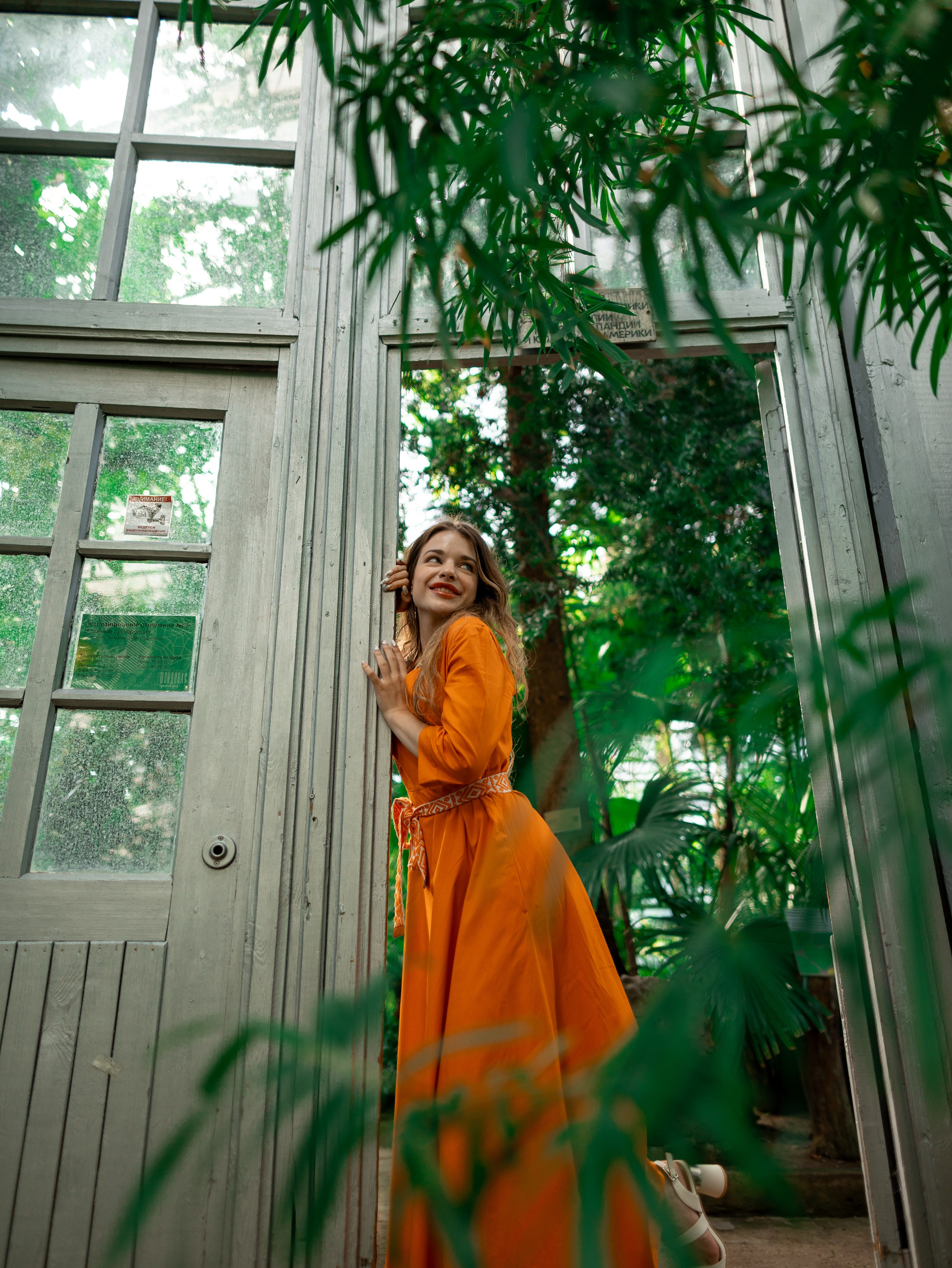 Девушка в оранжевом платье стоит на фоне зелени