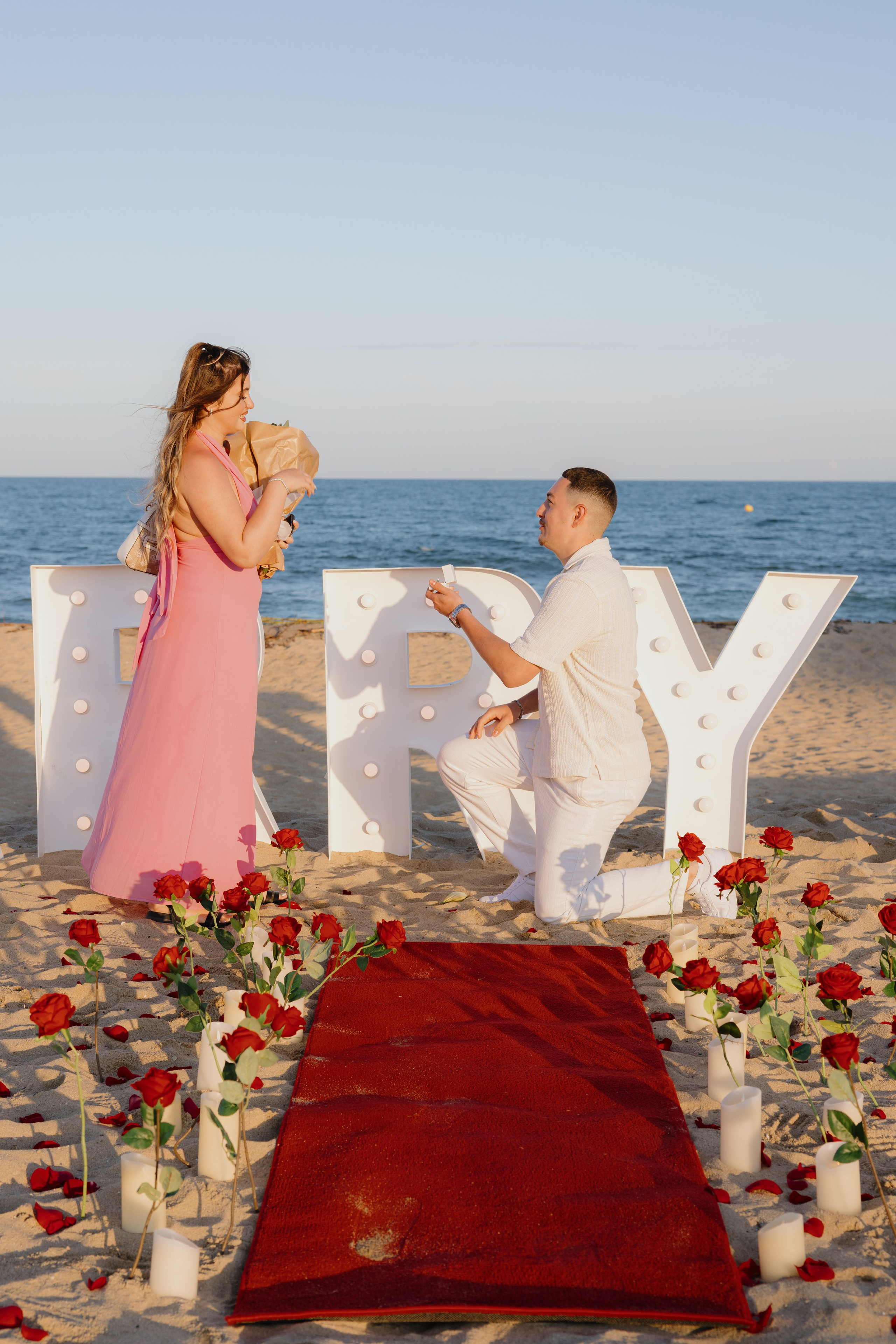 Marriage proposal at sunset on the beach — man on one knee holding an engagement ring