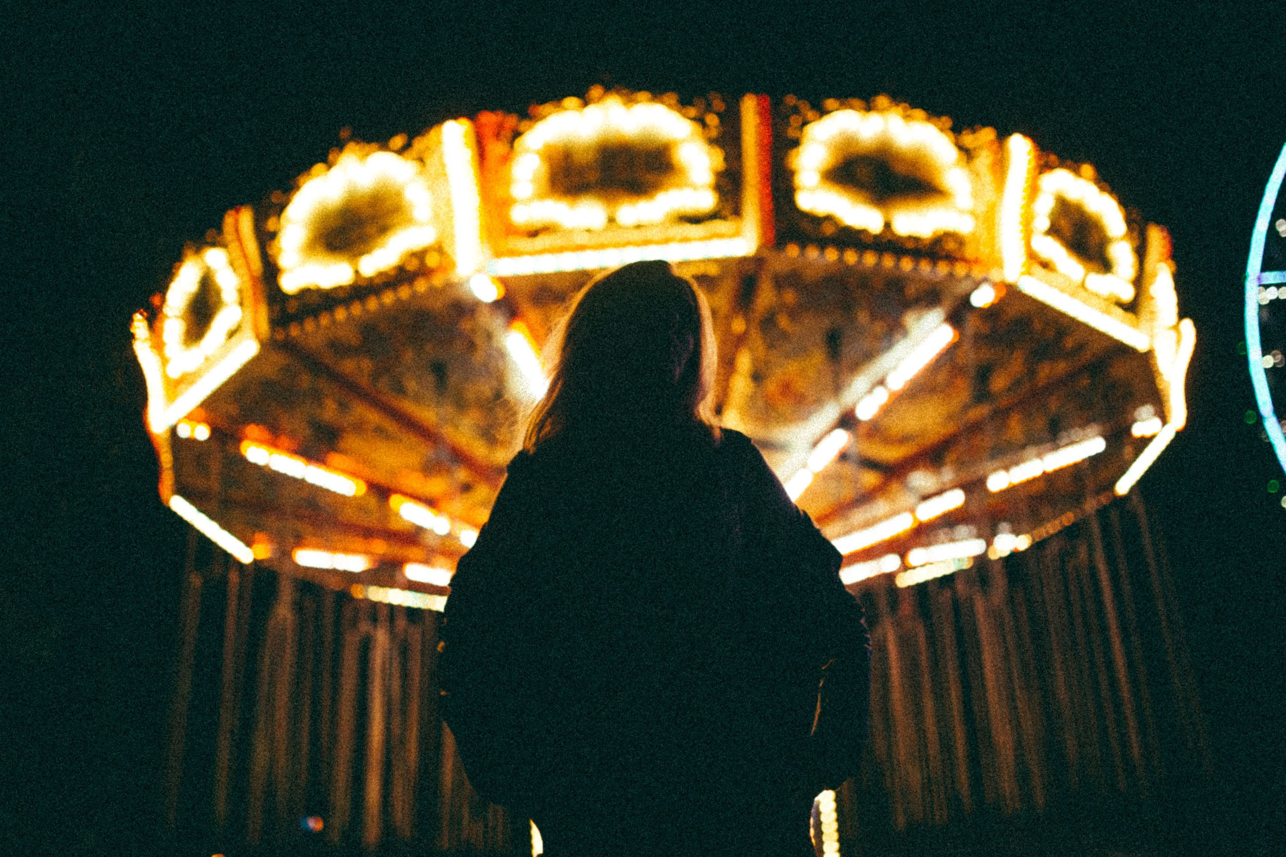 Темный женский силуэт на фоне светящейся в темноте карусели