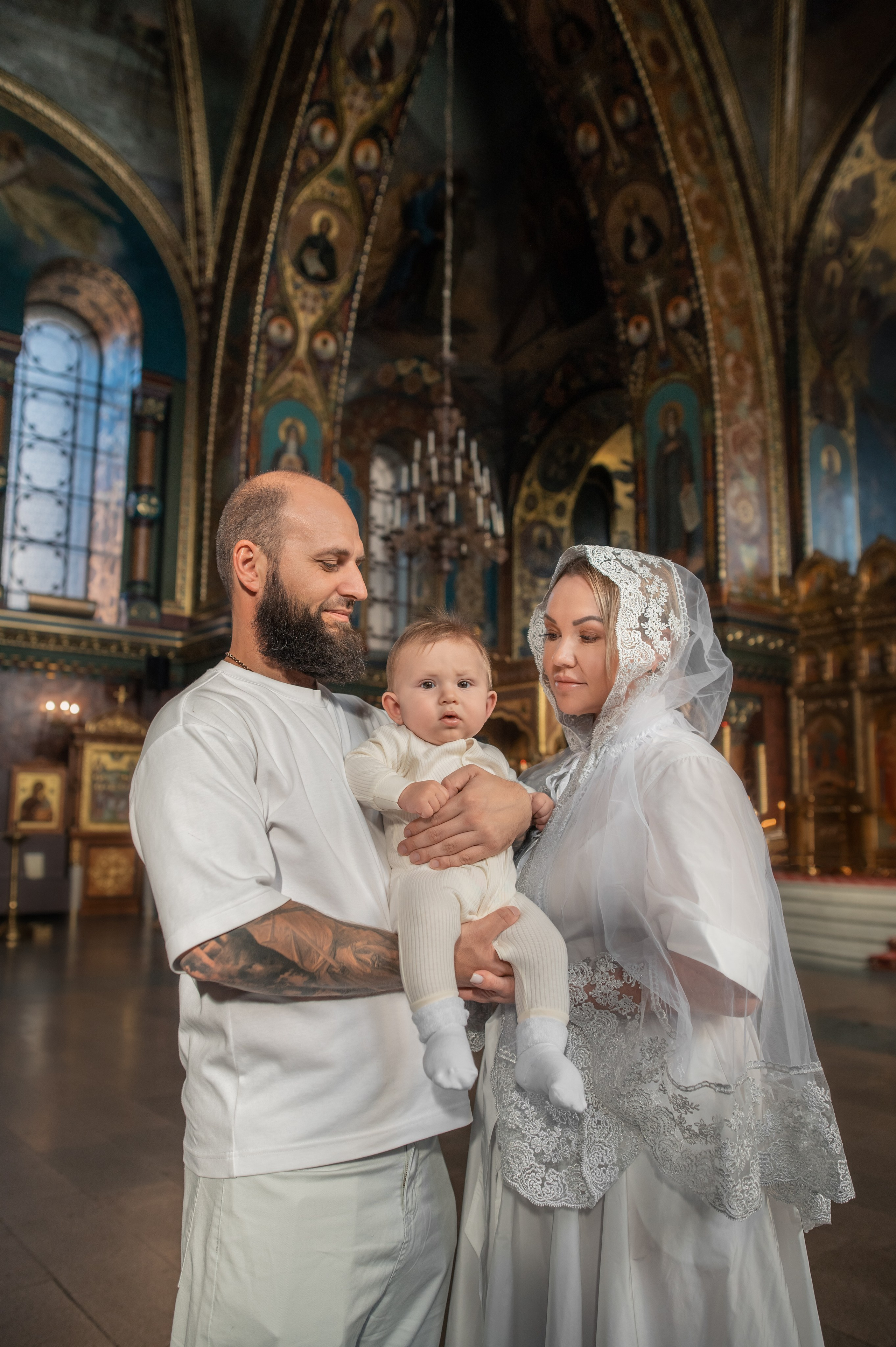 мама и папа улыбаются и держат малыша в Оптинском подворье Санкт-Петербурга