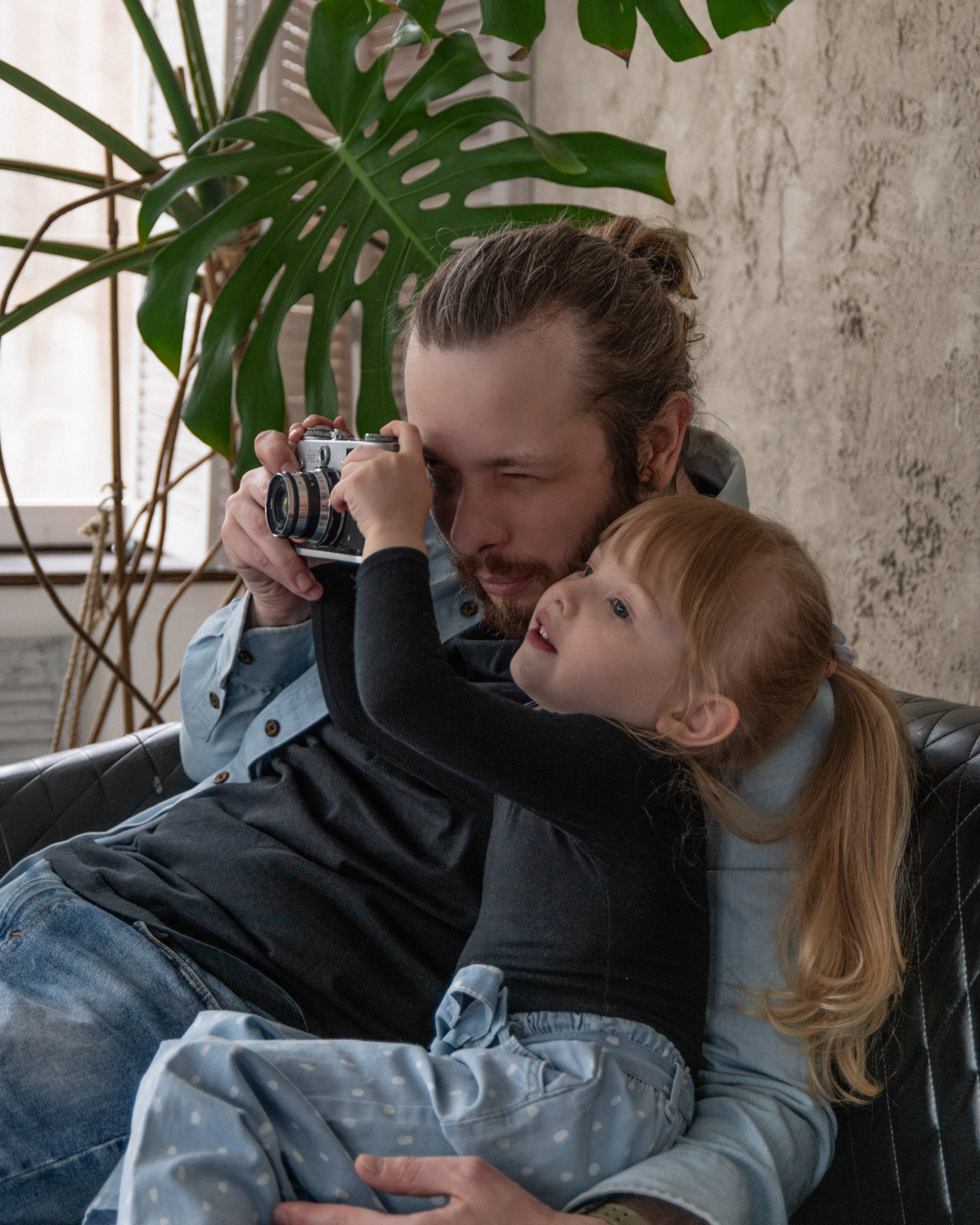 Отец показывает дочери, как пользоваться камерой — тёплая семейная сцена в скандинавском интерьере с живыми эмоциями.
