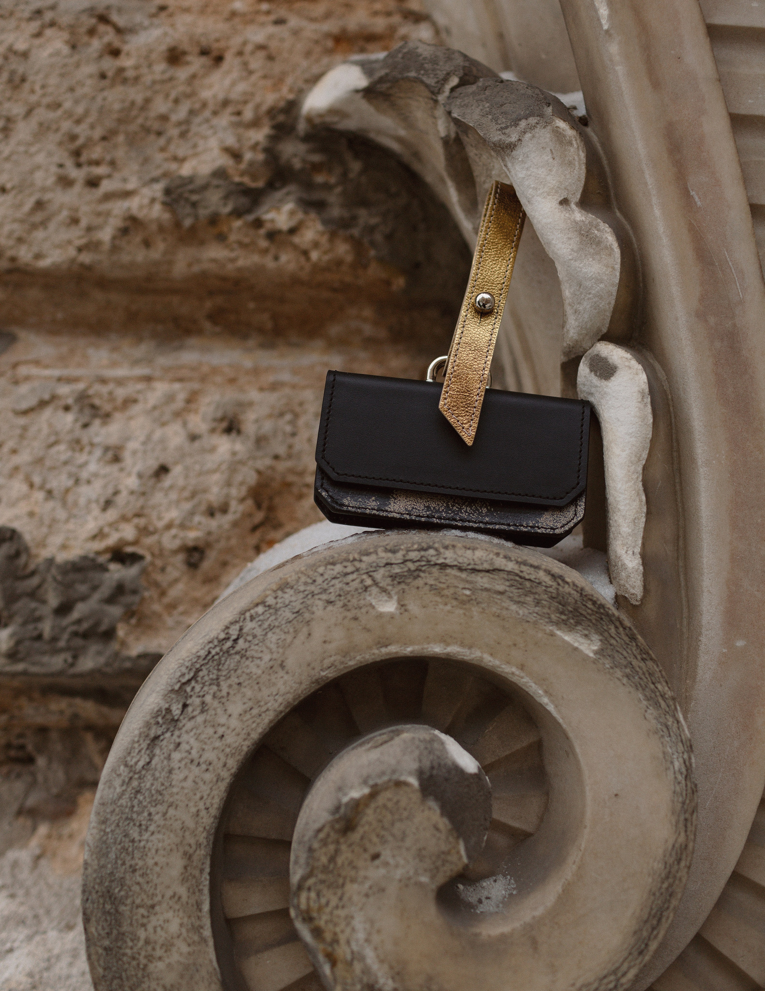 Предметная съемка маленькой черной сумочки с золотым ремешком рядом с архитектурой Санкт-Петербурга.