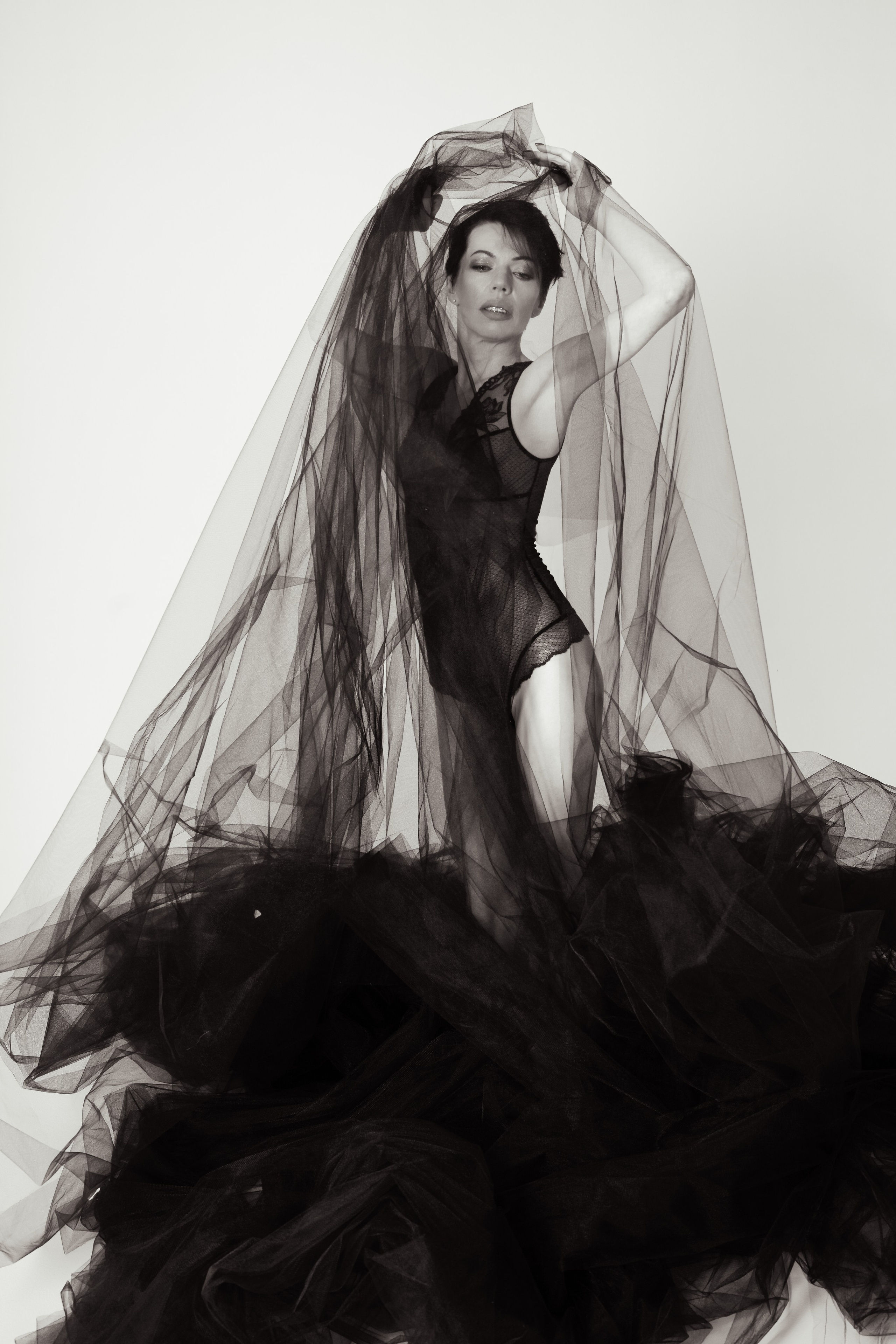 Молодая девушка в боди стоит на циклораме под облаками ткани Сатина