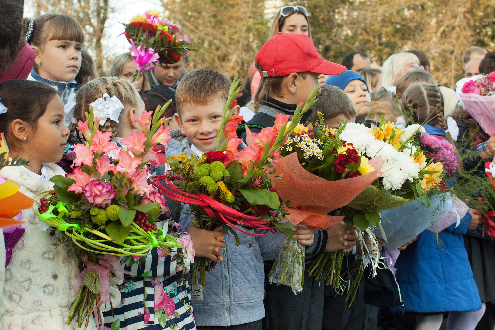 Первоклассники стоят на улице на линейке 1 сентября и держат большие букеты в руках.