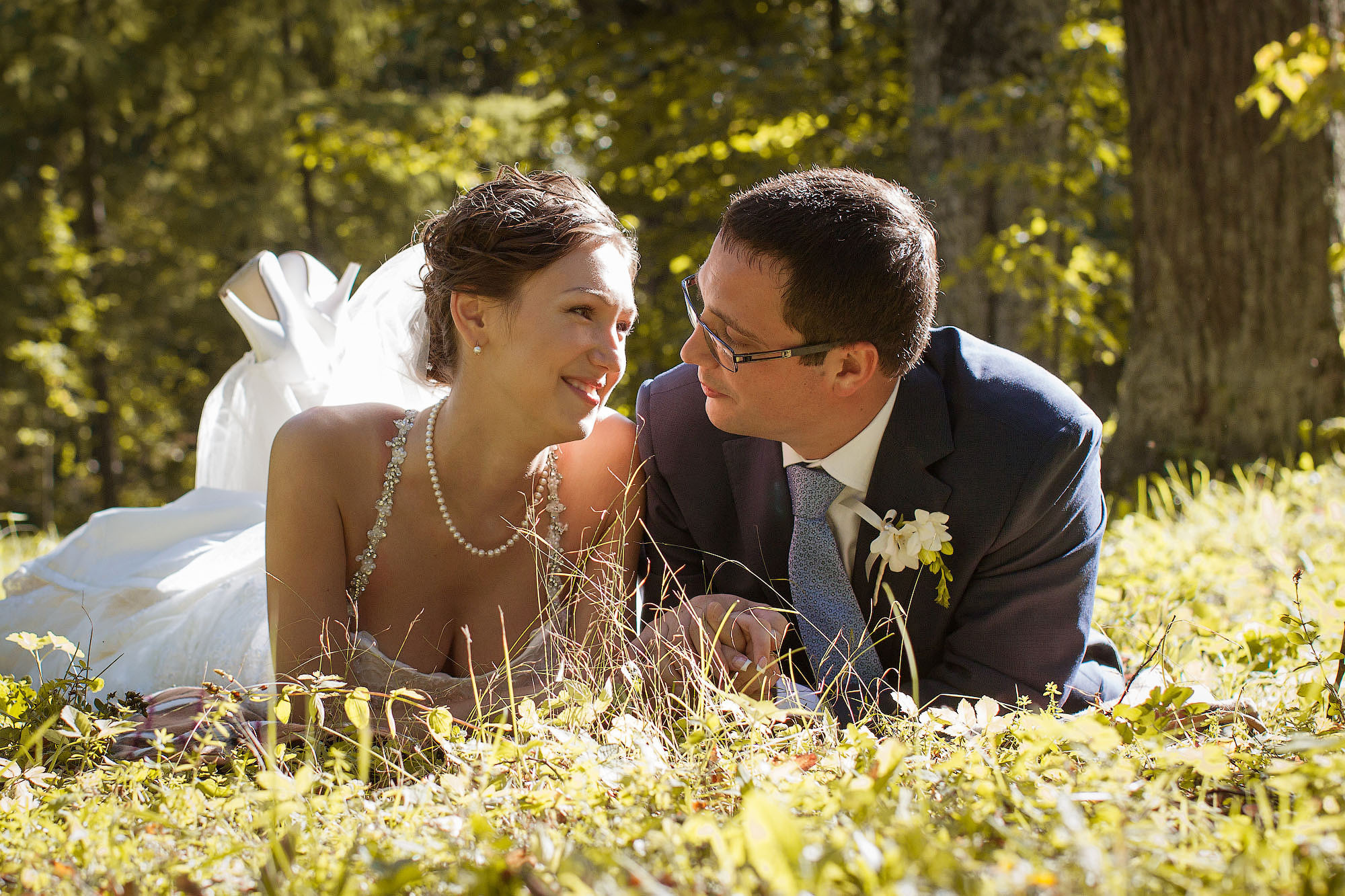 свадебное фото с женихом и невестой, которые лежат на животе на траве в солнечный день и смотрят друг на друга.