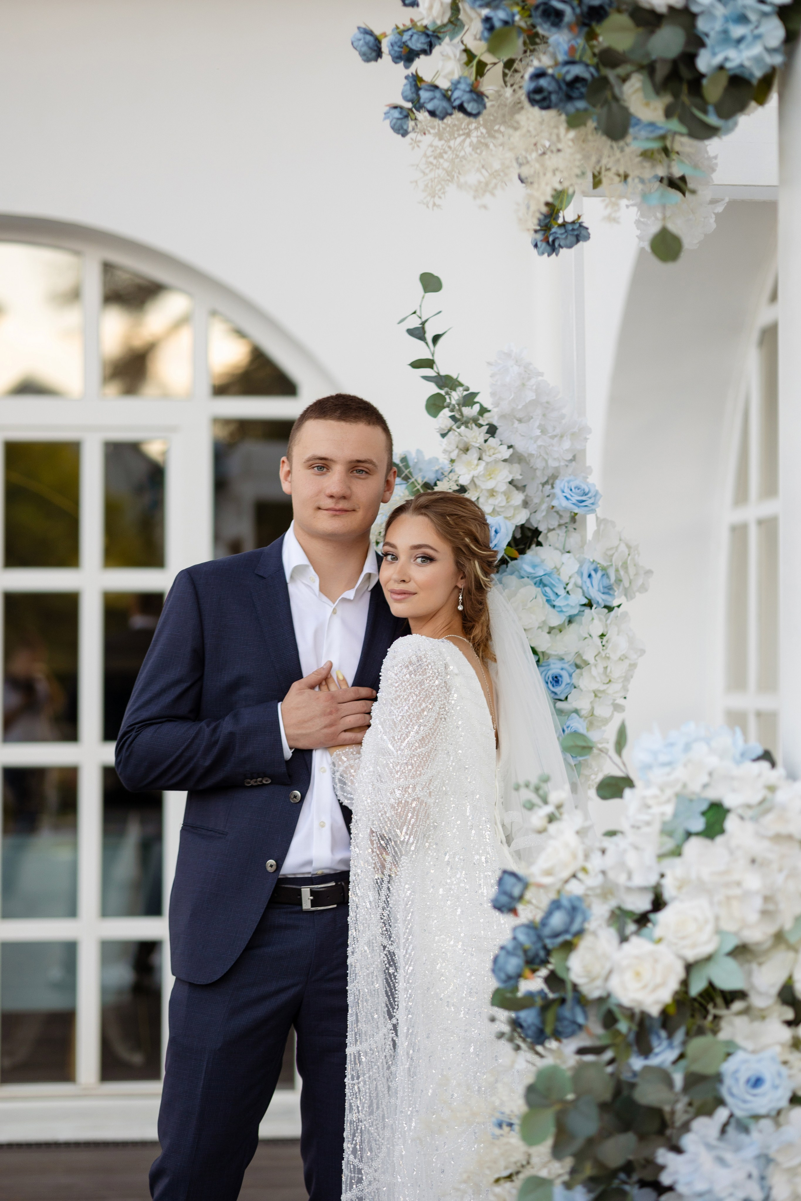 Молодые на фоне большого арочного окна.