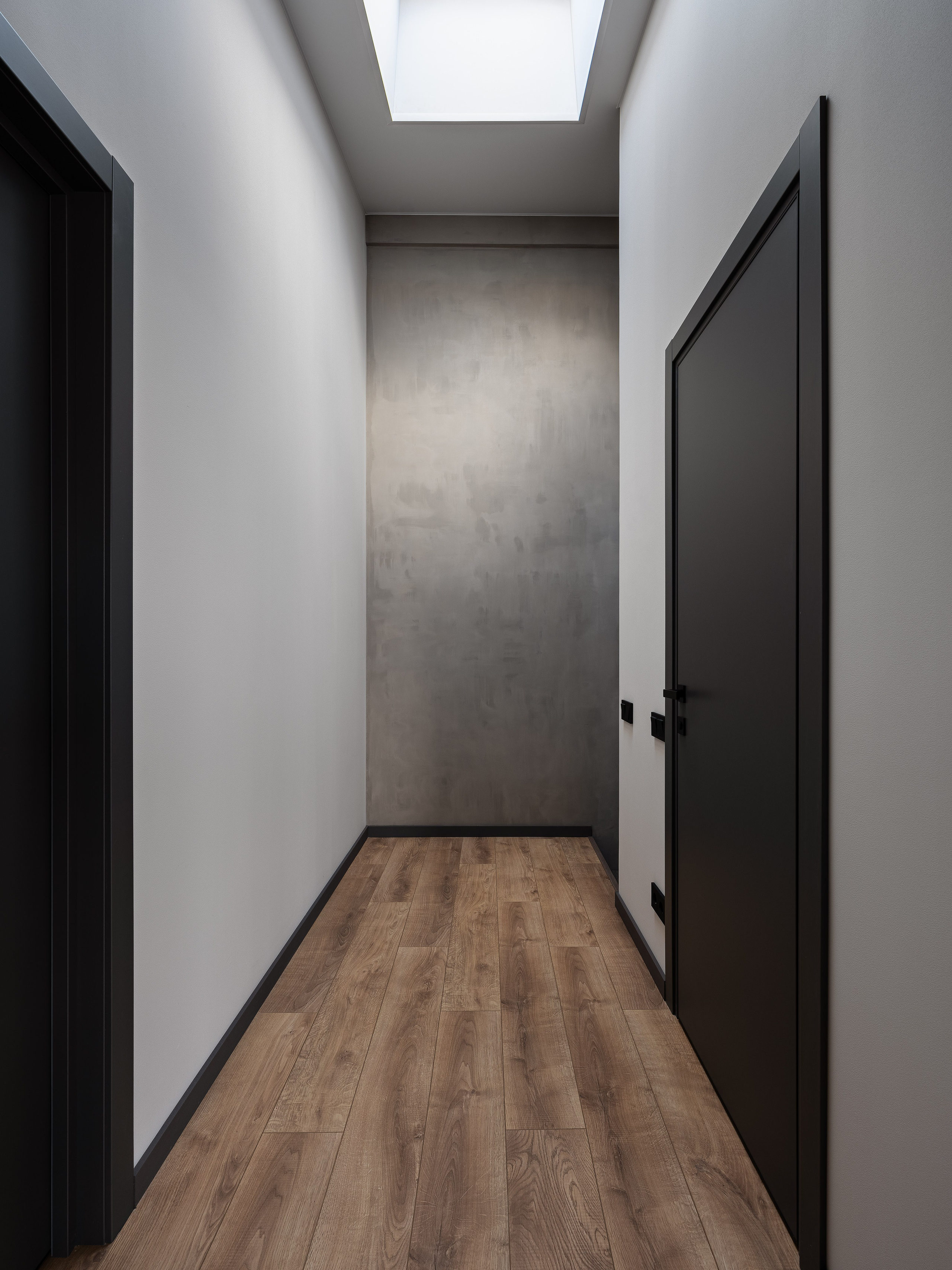 Светлый коридор с серой акцентной стеной и потолочным окном, наполняющим пространство естественным светом, деревянный пол подчёркивает уют. Дизайнер Екатерина Мищенко, фотограф Сергей Денисенко, современный минимализм.