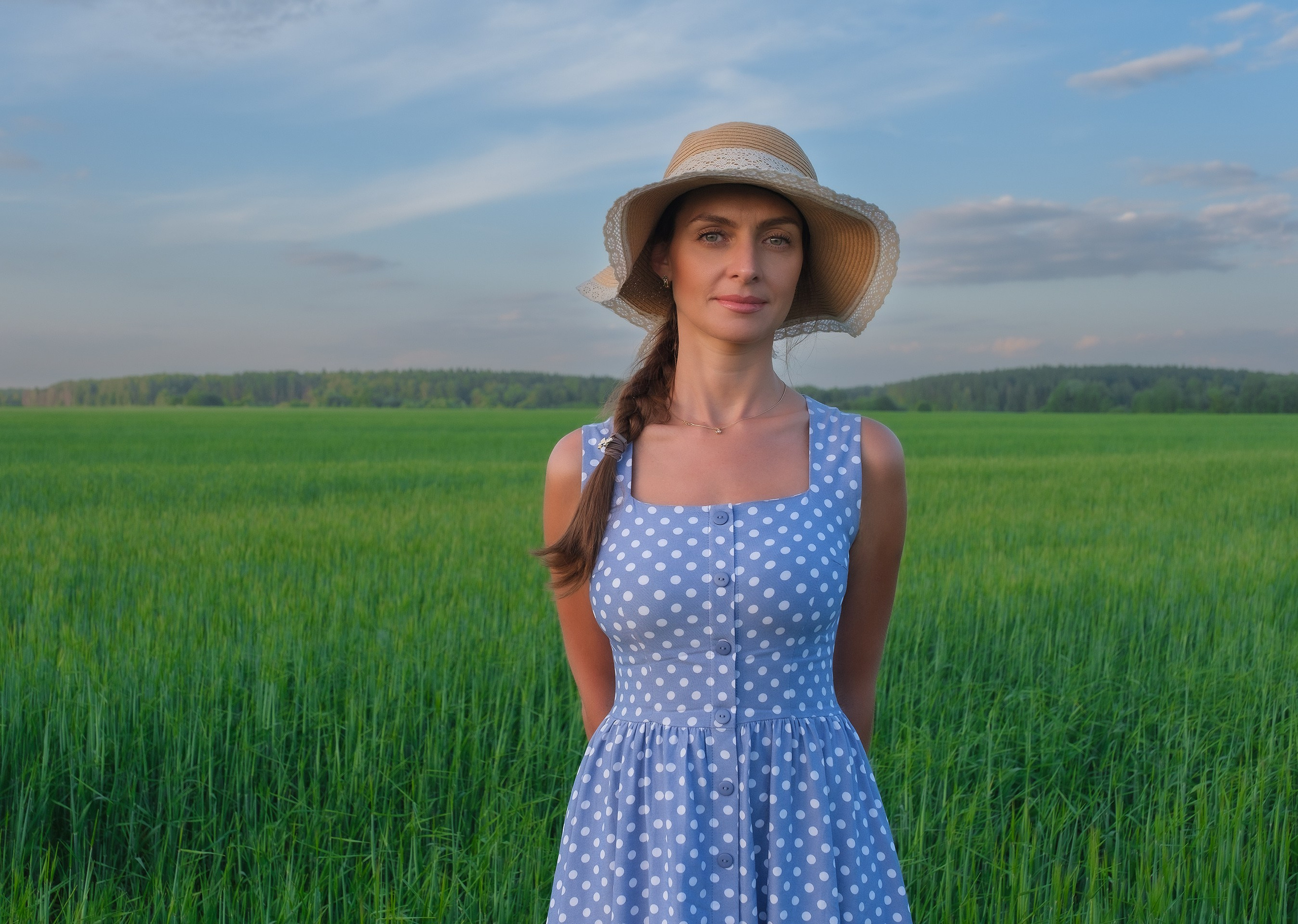 Фотосессия девушки в шляпке и сарафане на фоне поля и неба