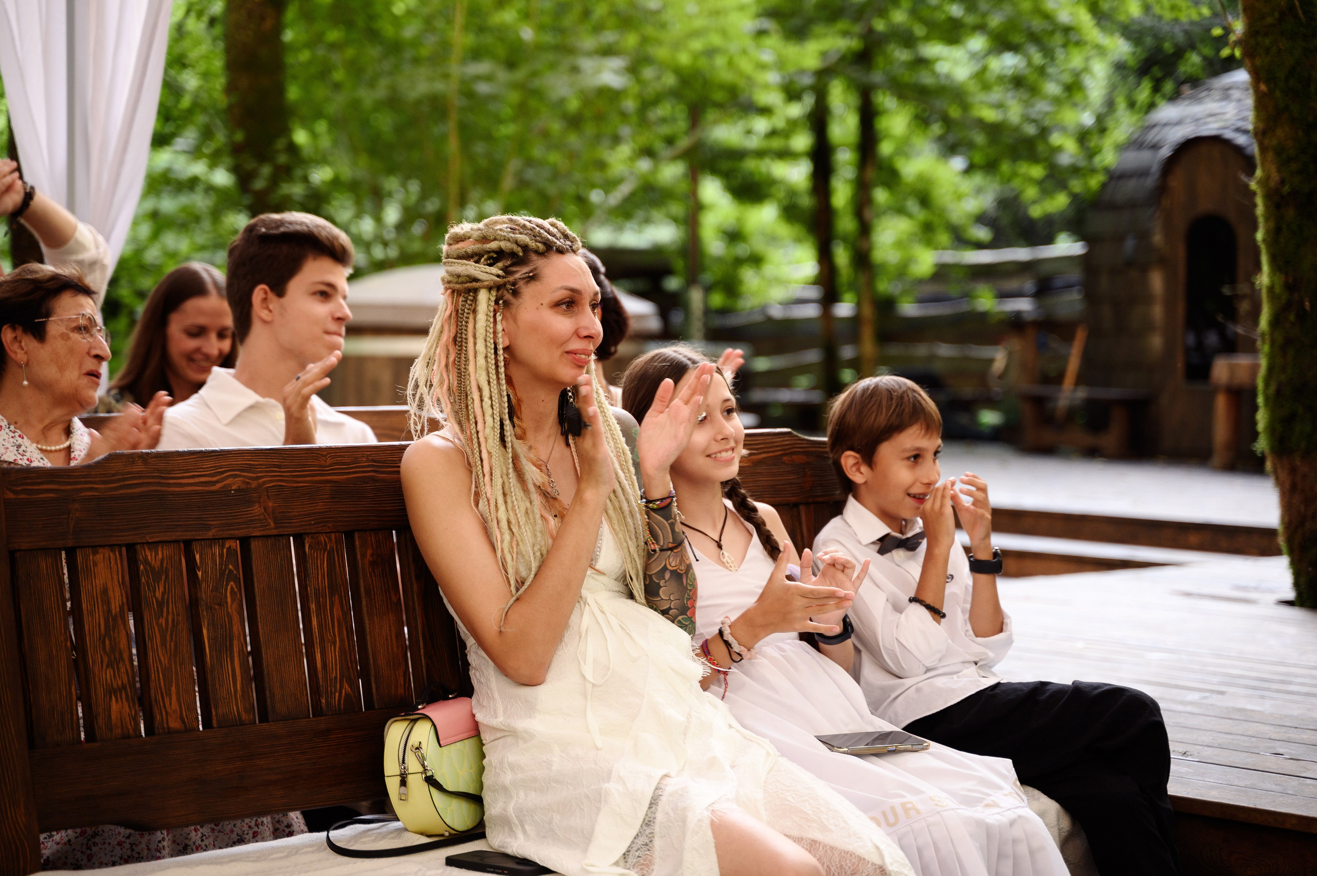 Женщина сидит на лавочке этот церемония свадебная они хлопают рядом с ней двое детей девочка и мальчик видимо ждут когда выйдут молодые