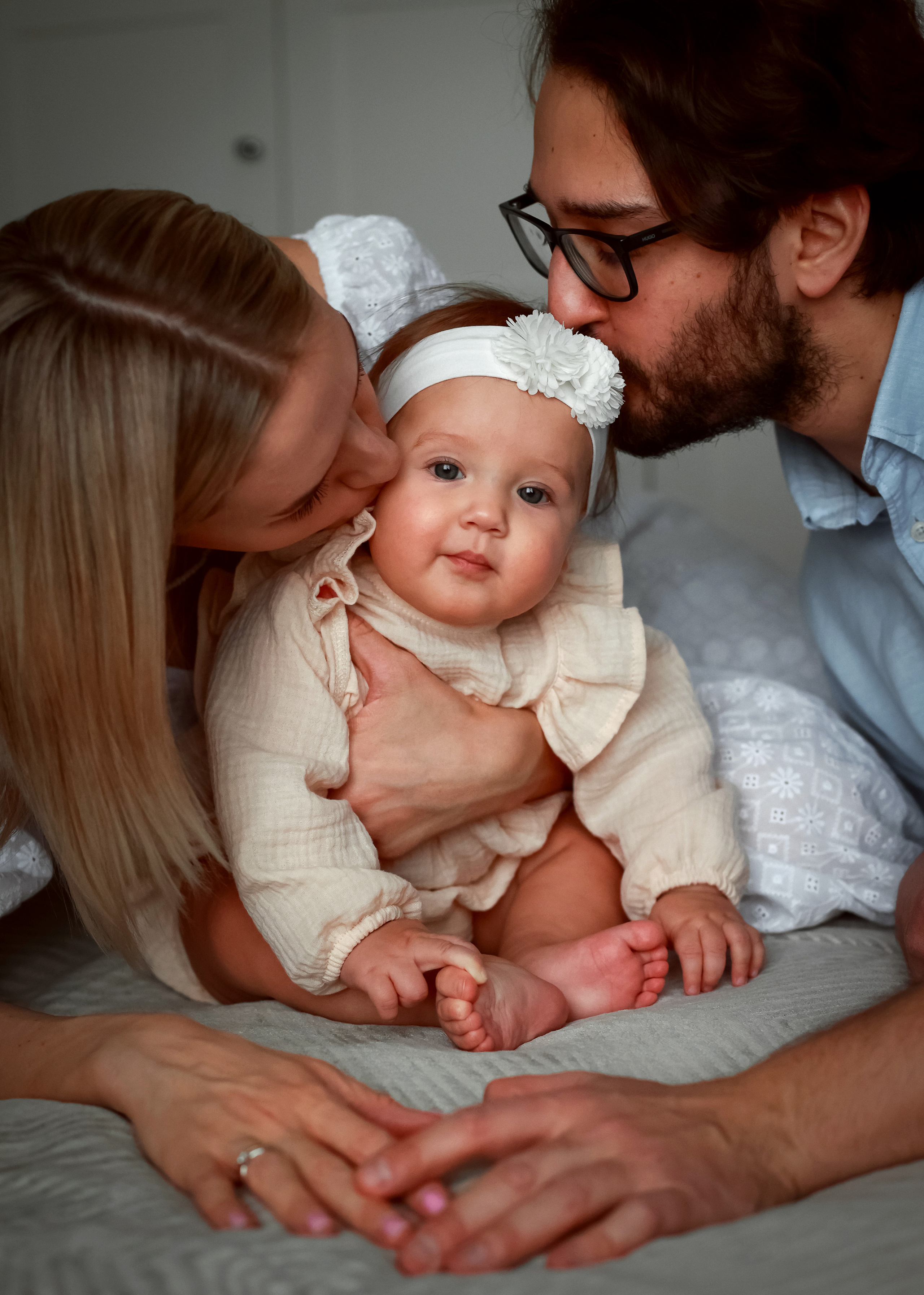 Мама и папа нежно целуют малыша в макушку. 