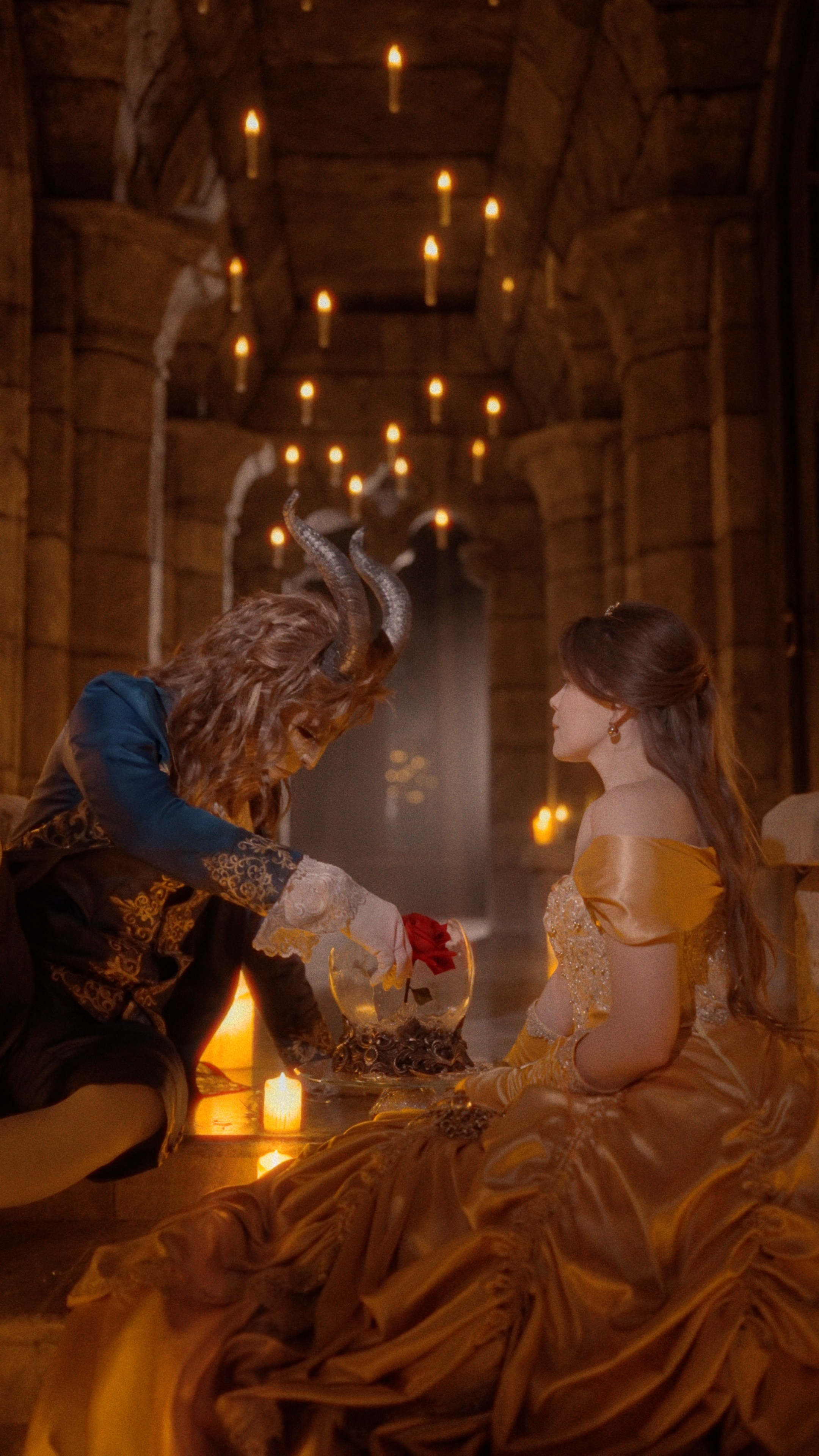 Сцена в стиле «Красавицы и Чудовища» в замке Гарибальди: мужчина в сказочном костюме протягивает розу девушке в золотом платье при свечах.