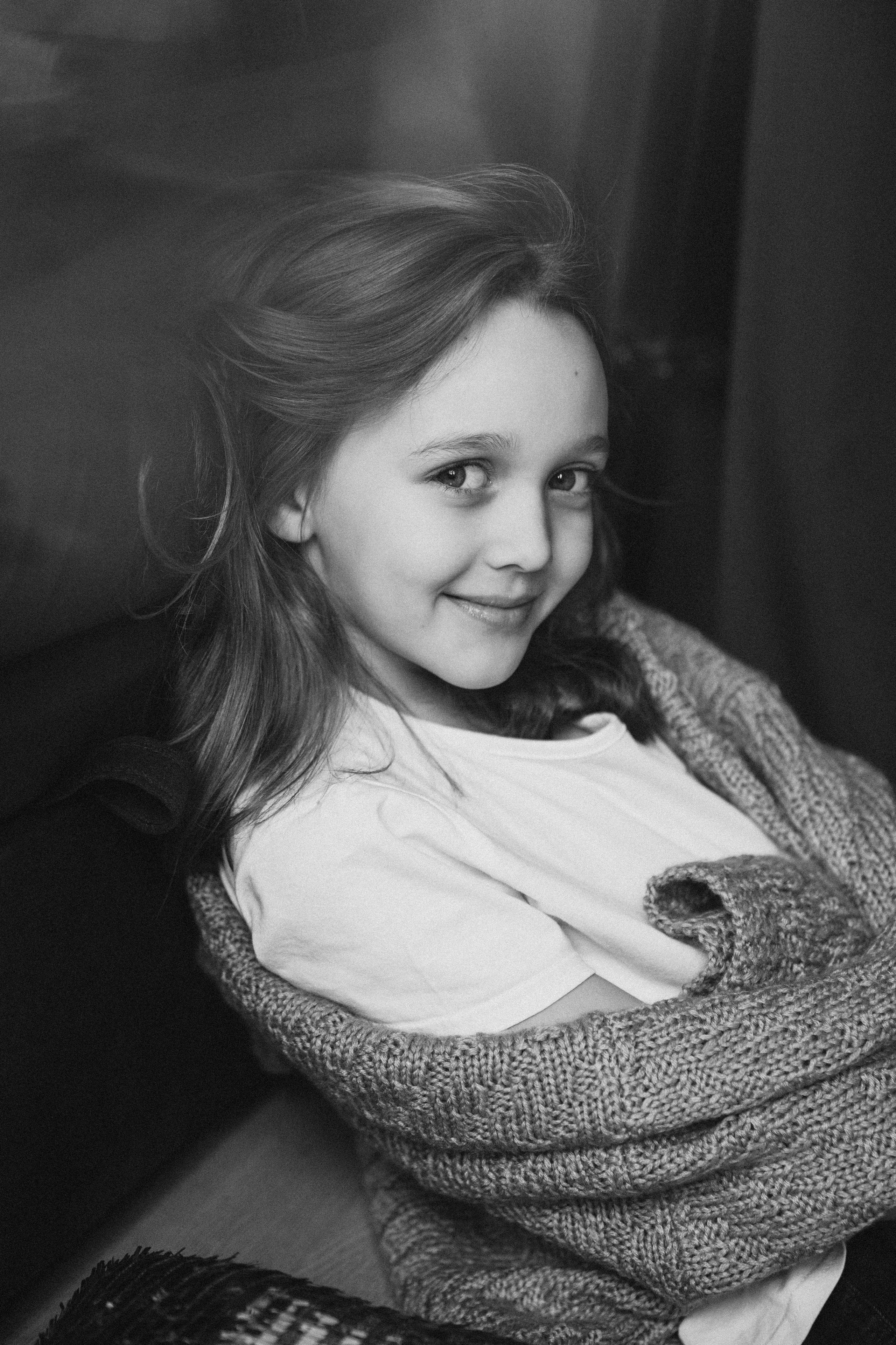 маленькая милая девочка в белой майке и свитере  сидит на полу около дивана в теплой комнате весной