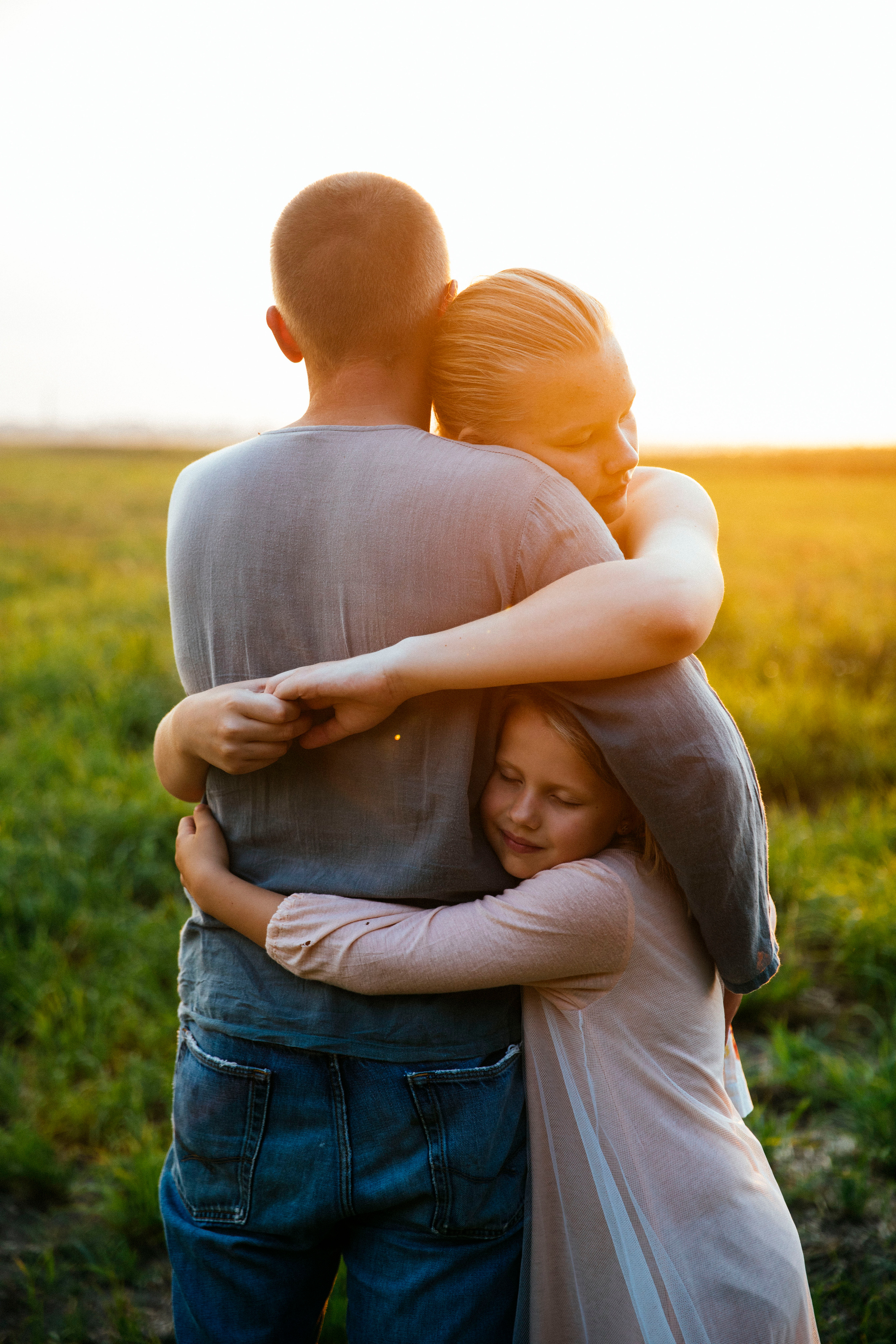 молодой папа  со своими дочками гуляет летом в поле на закате где цветут красивые одуванчики 