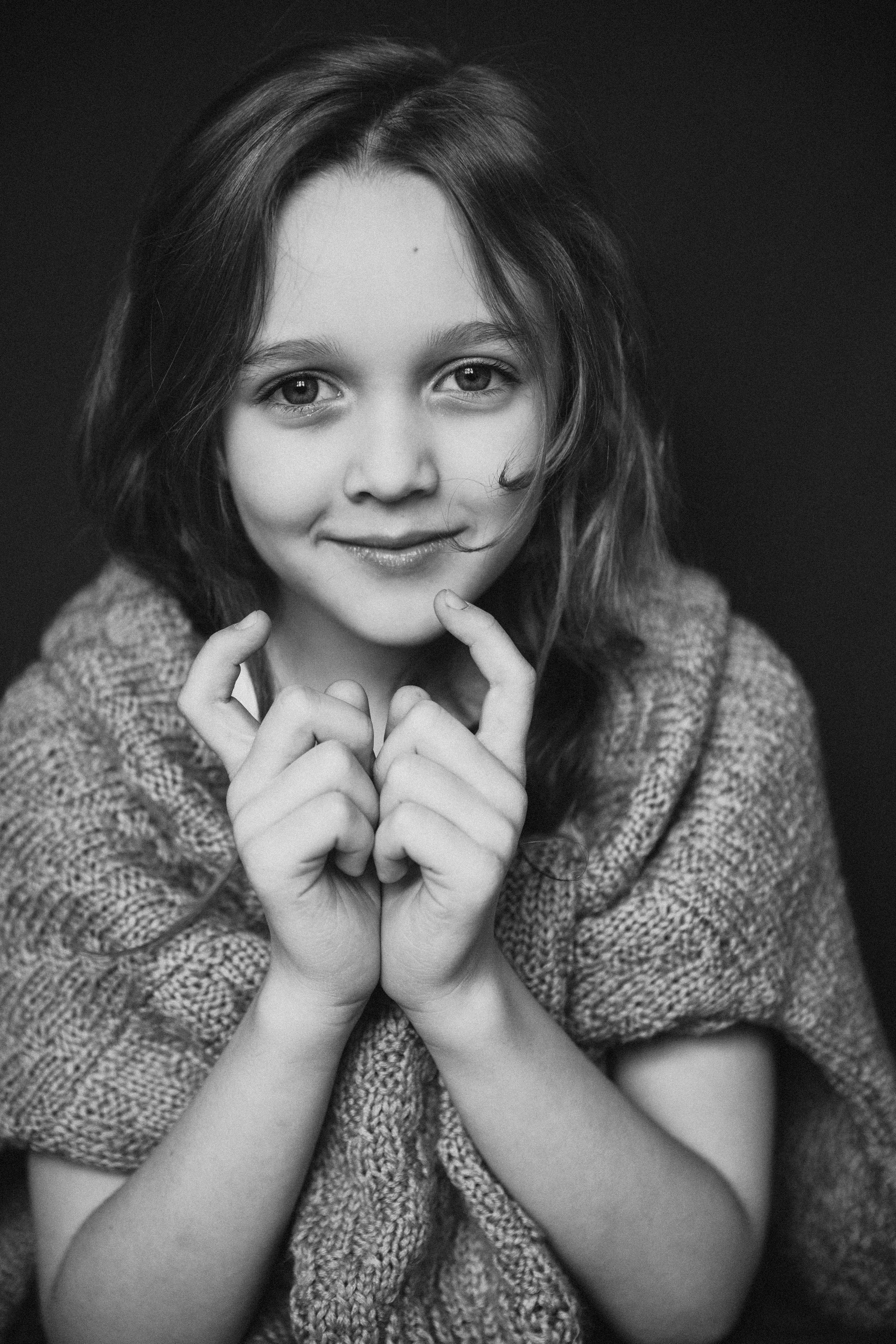 Красивая маленькая девочка в свитере улыбается и смотрит в окно