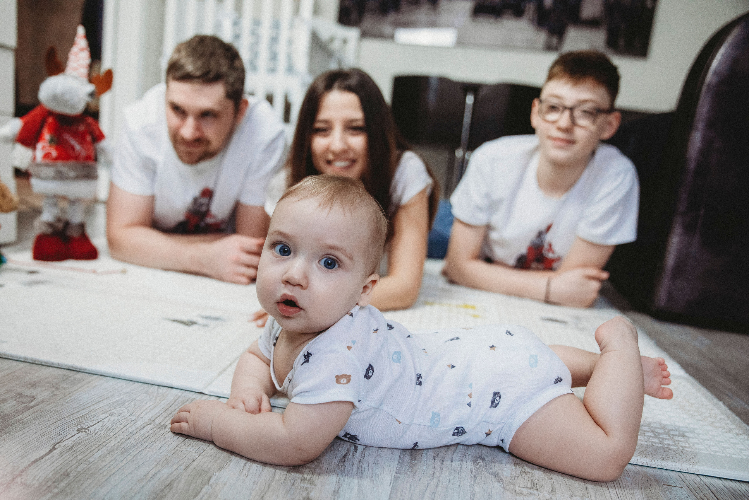 маленький ребеночек ползет по полу дома а за ним наблюдает его семья