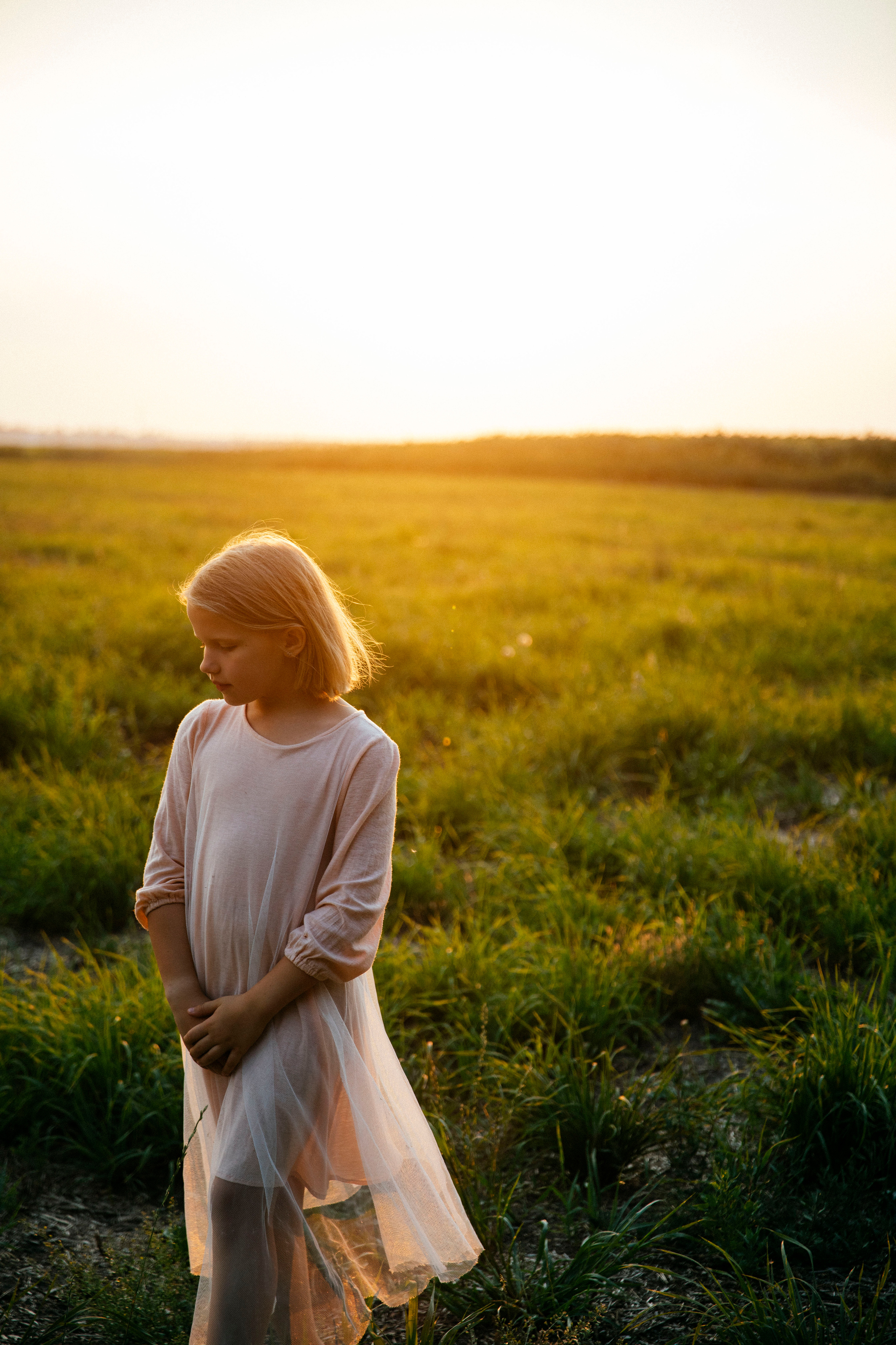 Красивая  девочка в воздушном платье гуляет по полю летним теплым вечером на закате