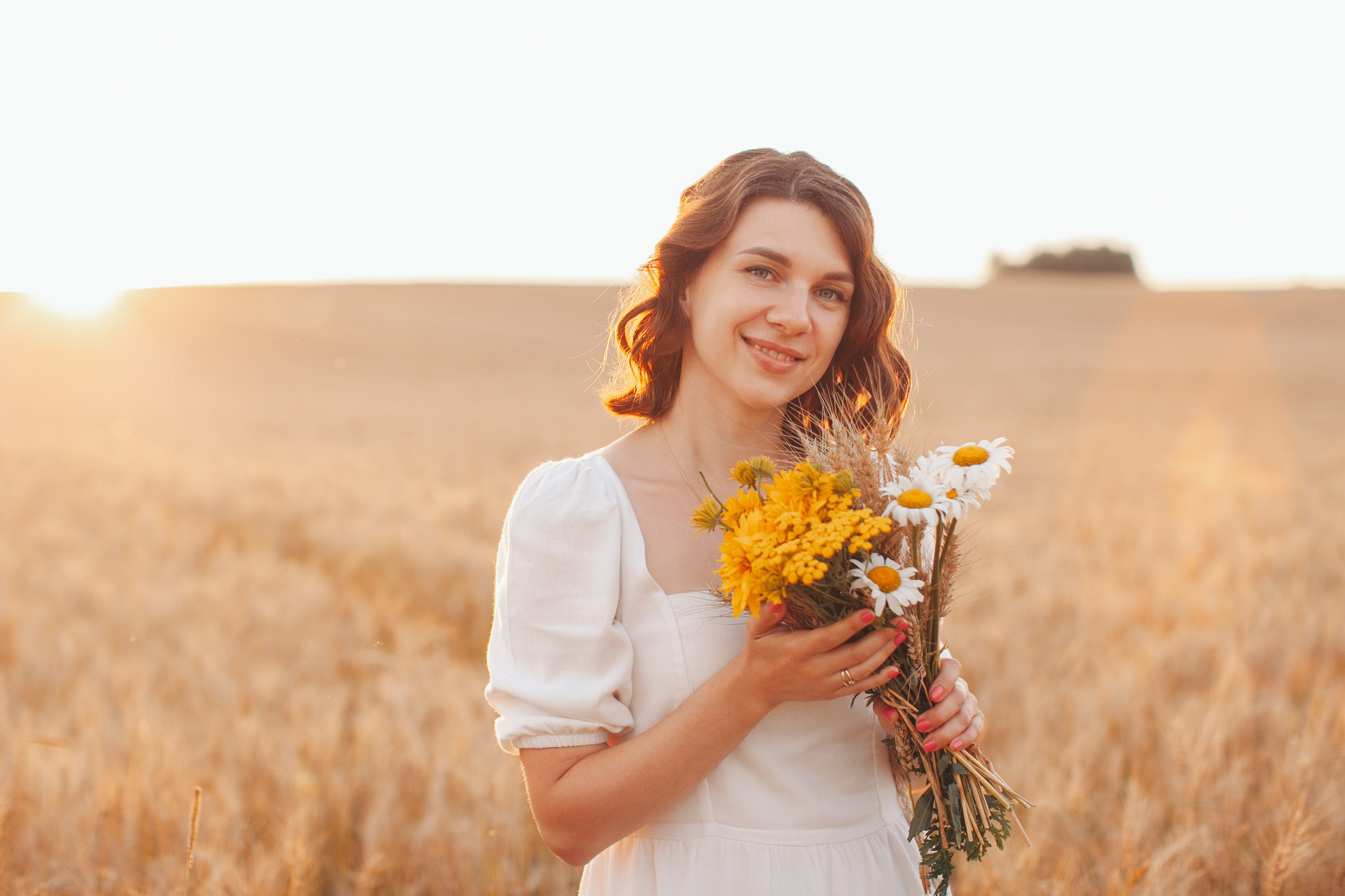 Кудрявая девушка на поле с букетом полевых цветов на фоне пшеничного поля