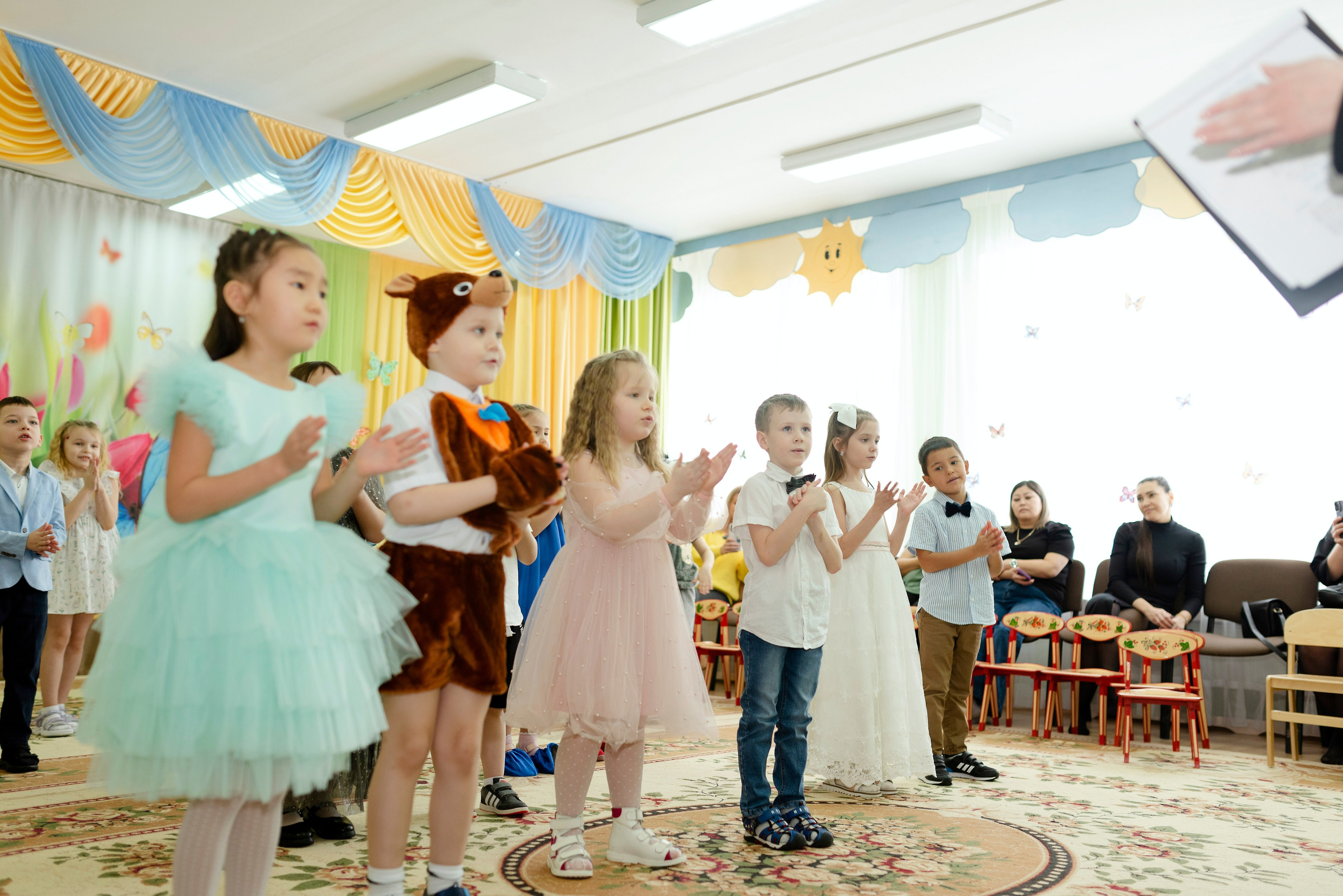 Дети танцуют веселый танец в праздничных костюмах на утреннике 8 марта в детском саду.