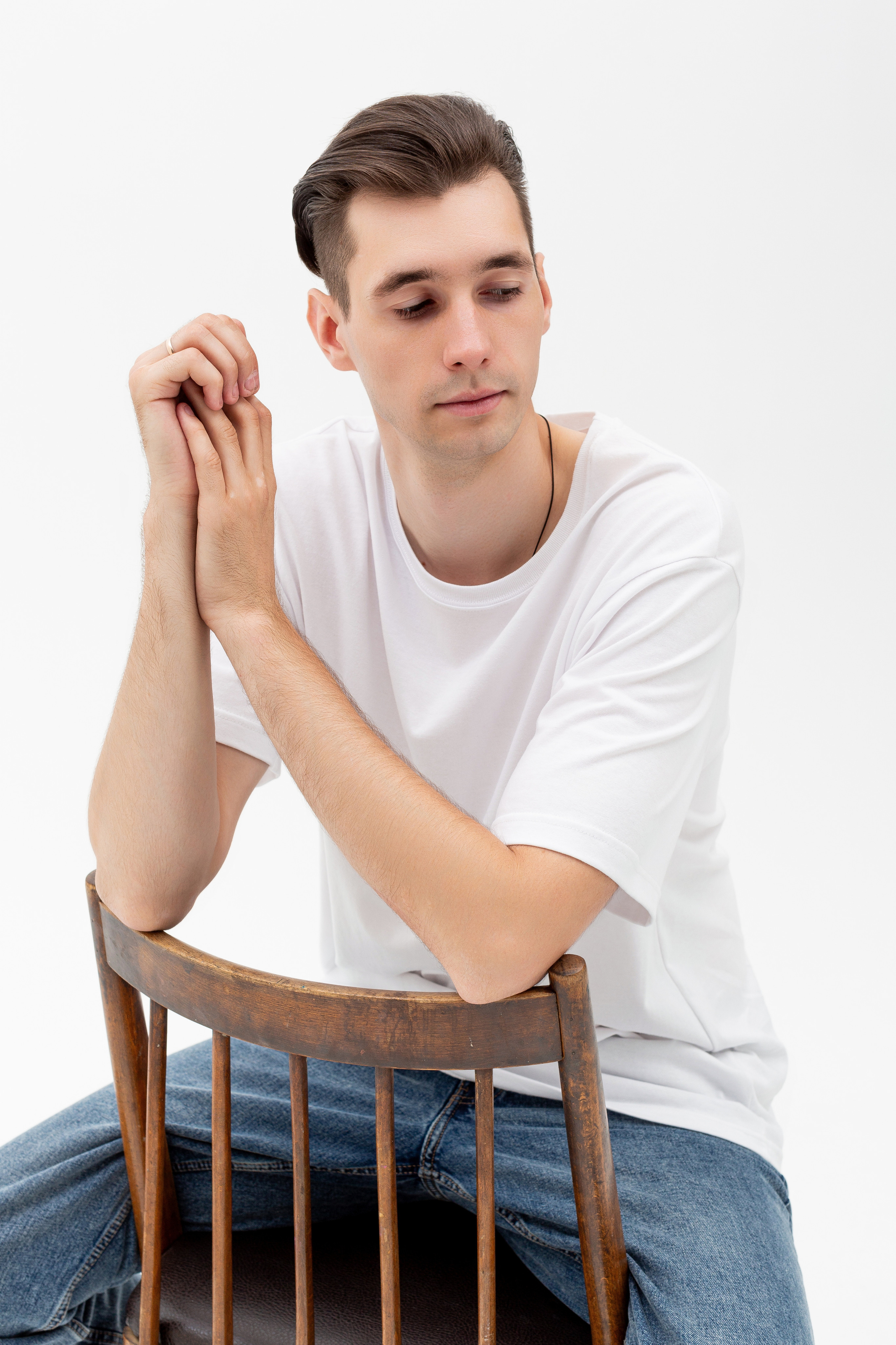 Студийный портрет мужчины сидящем на стуле, портрет 2/3, в белой футболке и джинсах на белом фоне