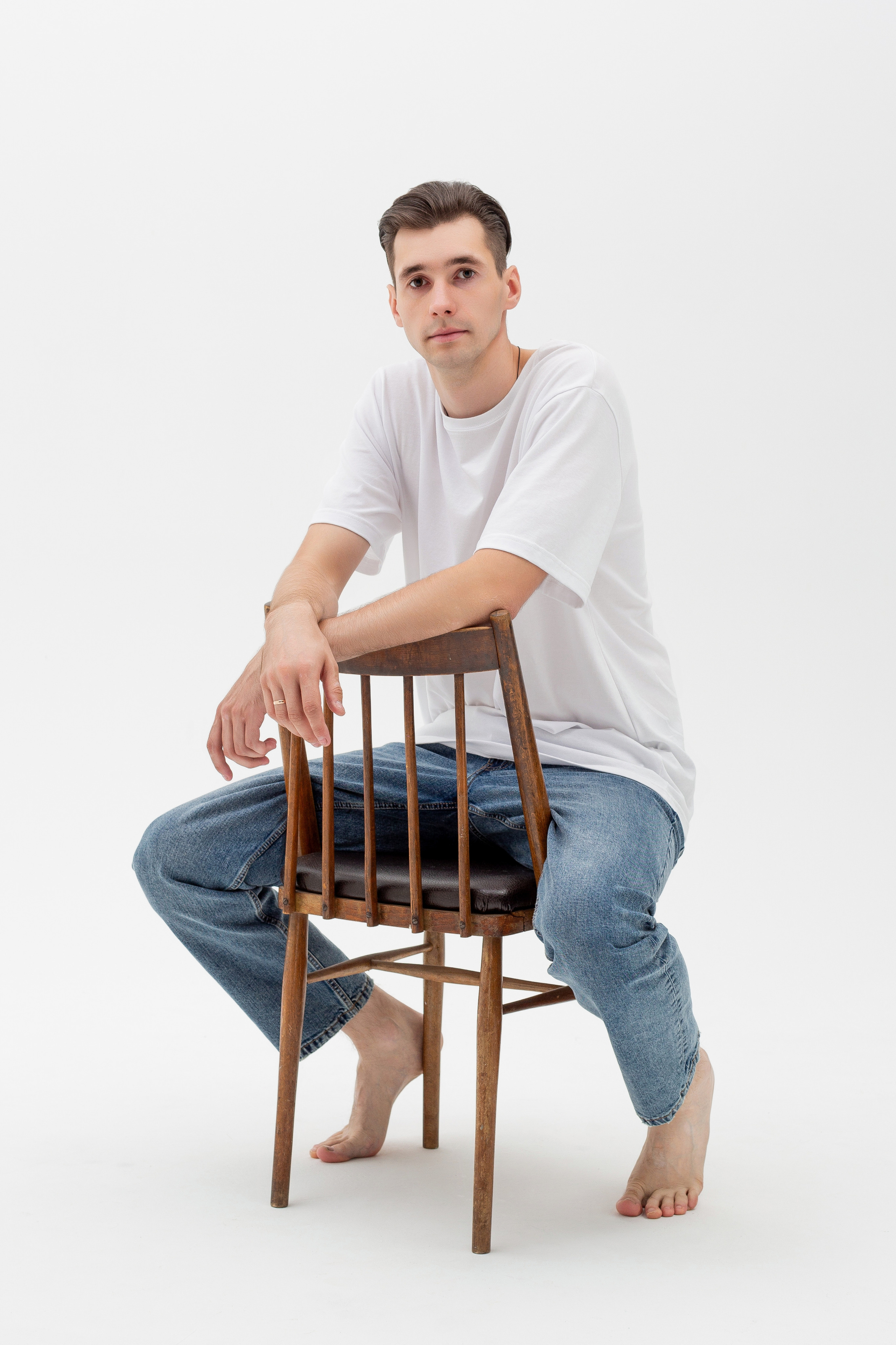 Студийный портрет мужчины сидящем на стуле, ростовой портрет, в белой футболке и джинсах на белом фоне