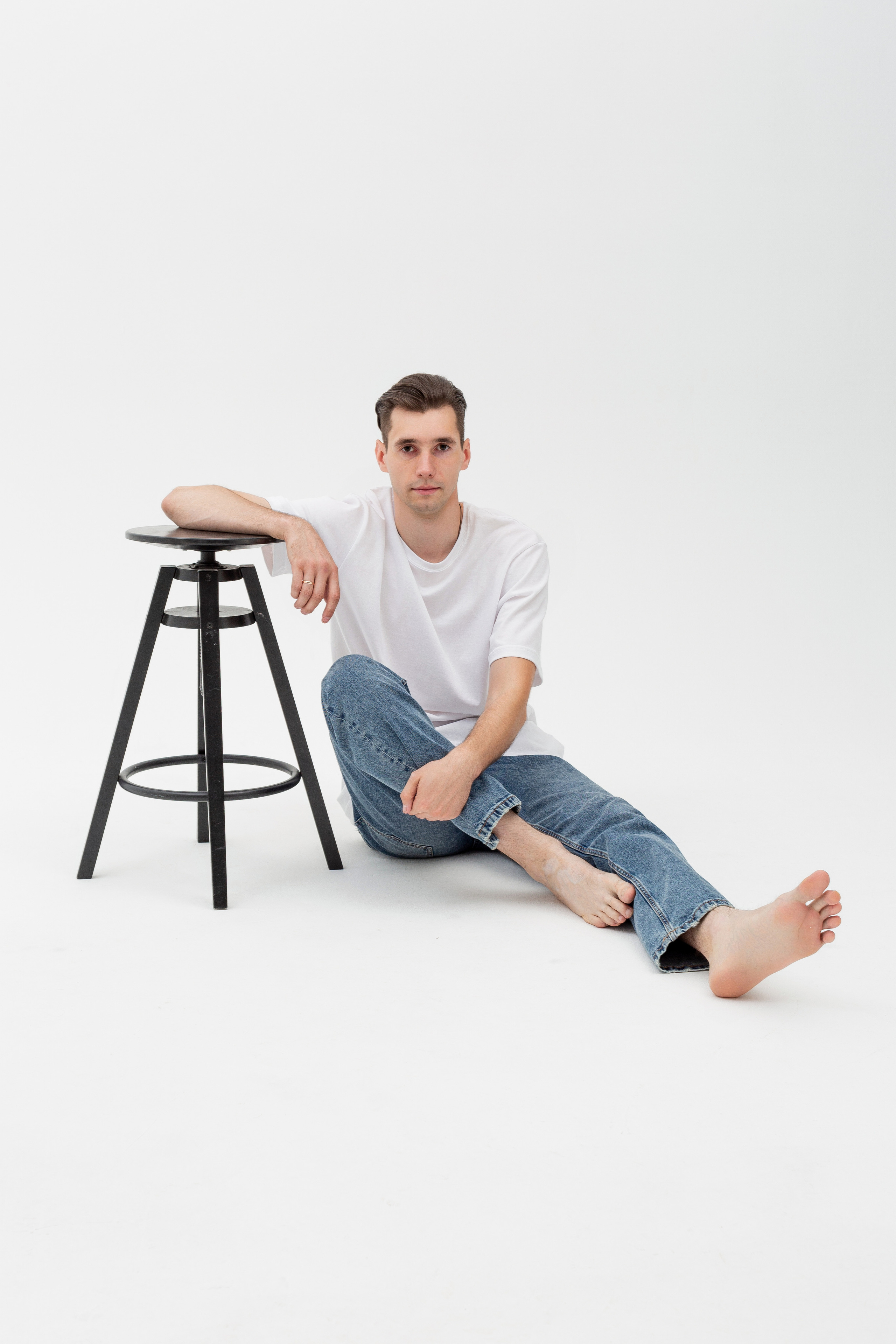 Студийный портрет мужчины сидящем на стуле, ростовой портрет, в белой футболке и джинсах на белом фоне