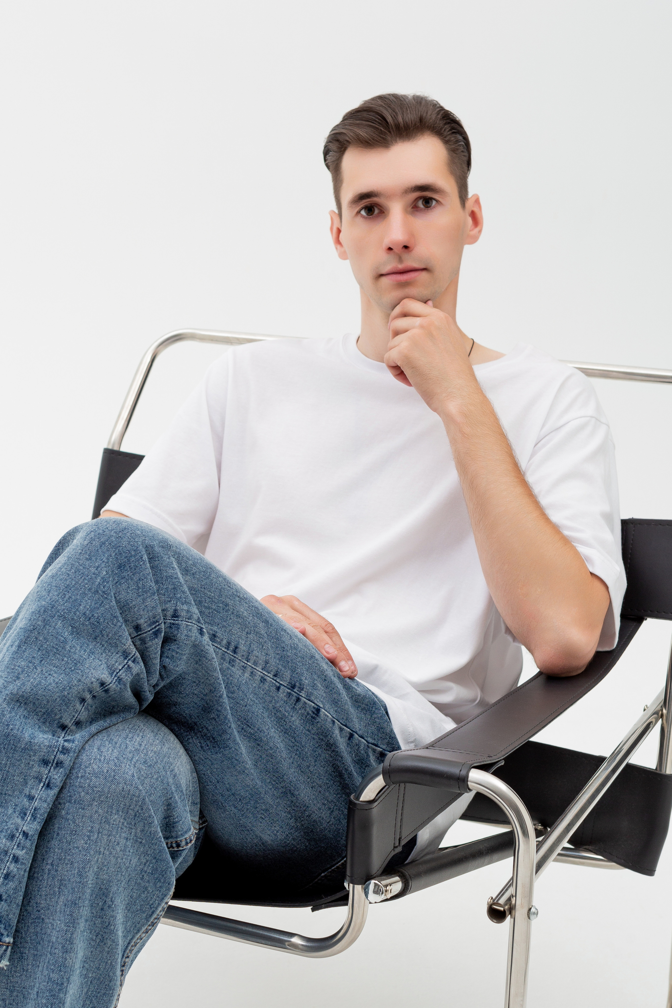Студийный портрет мужчины сидящем на стуле, портрет 2/3, в белой футболке и джинсах на белом фоне
