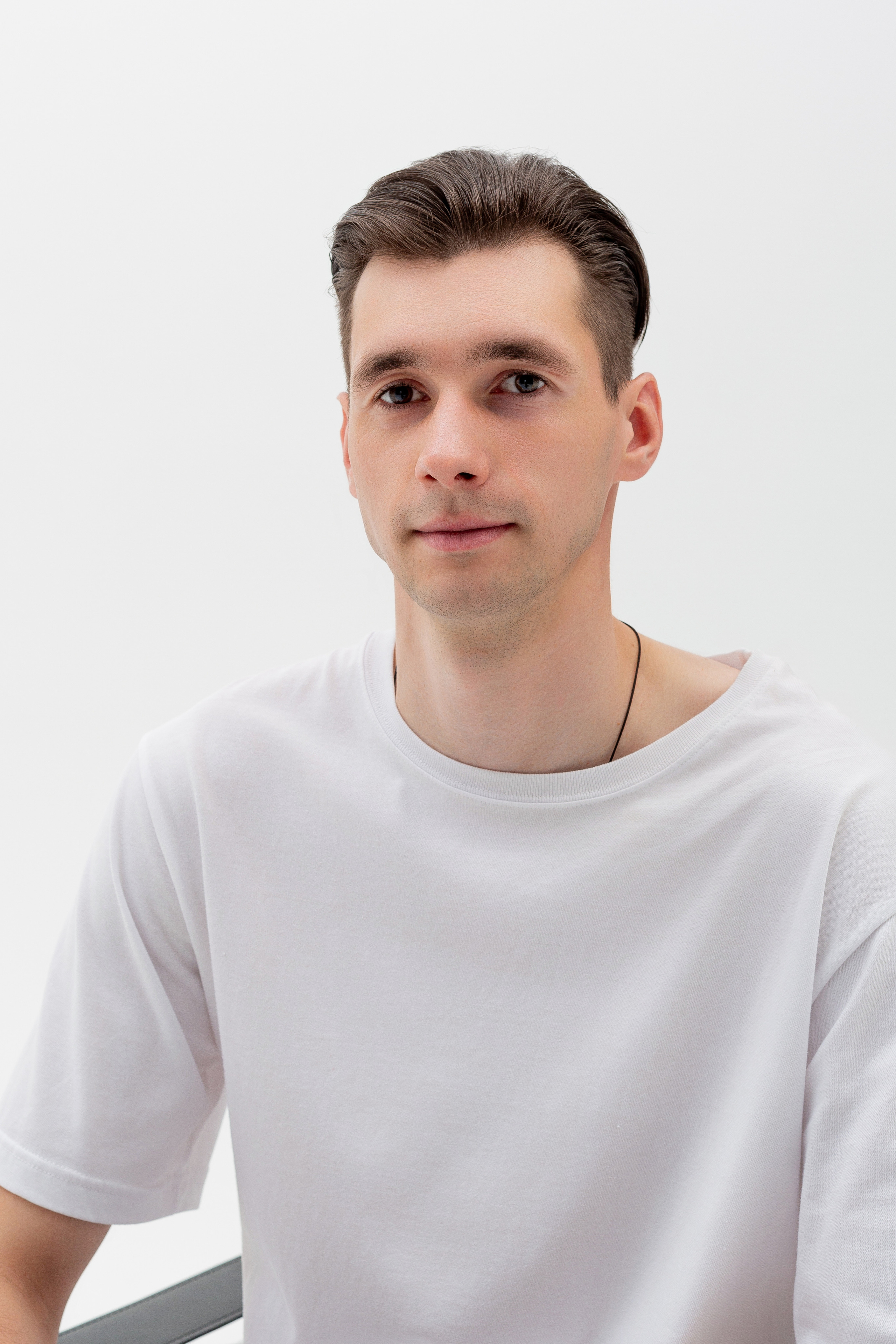 Студийный портрет мужчины сидящем на стуле, портрет 1/3, в белой футболке и джинсах на белом фоне