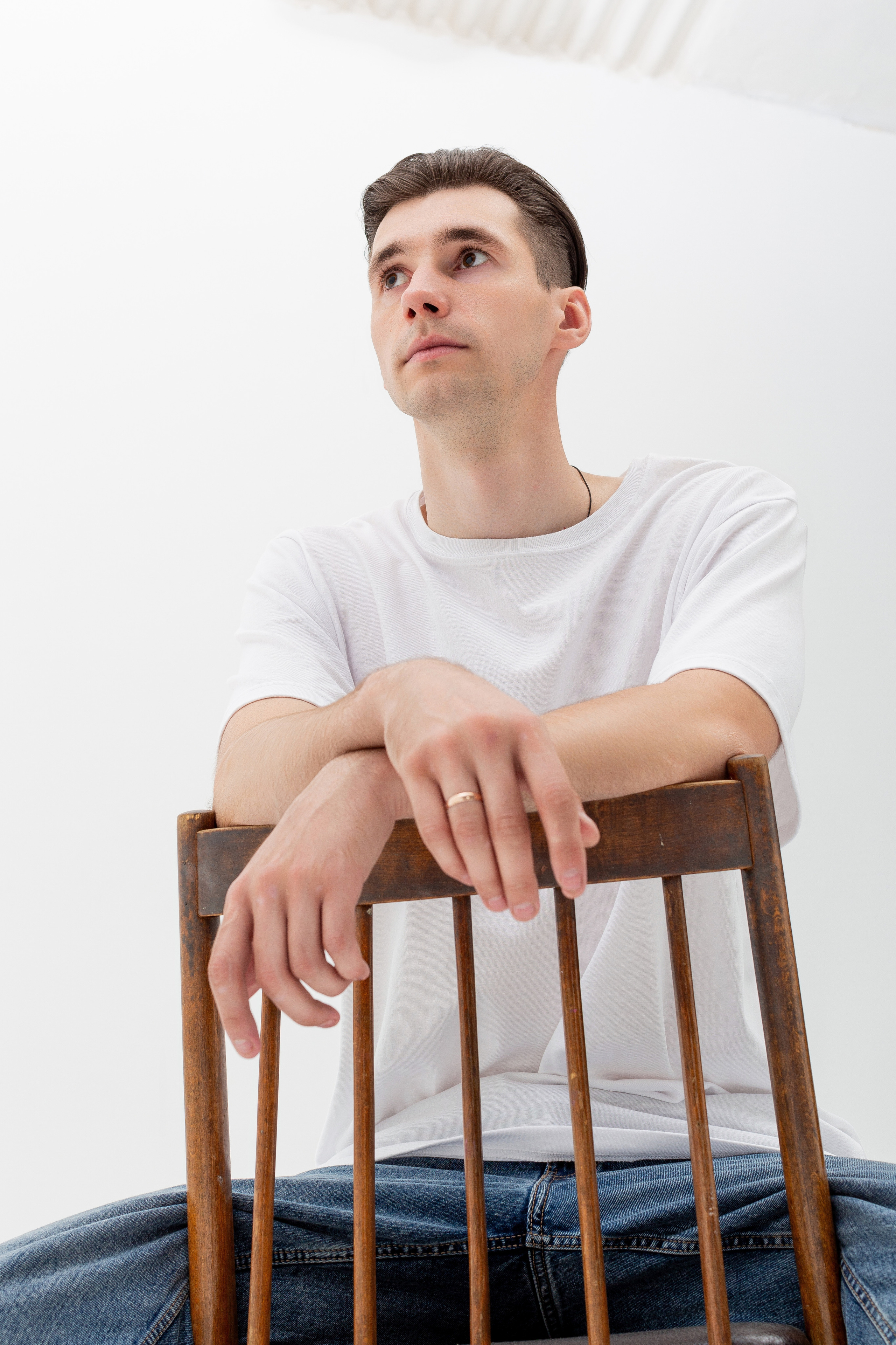 Студийный портрет мужчины сидящем на стуле, портрет 2/3, в белой футболке и джинсах на белом фоне
