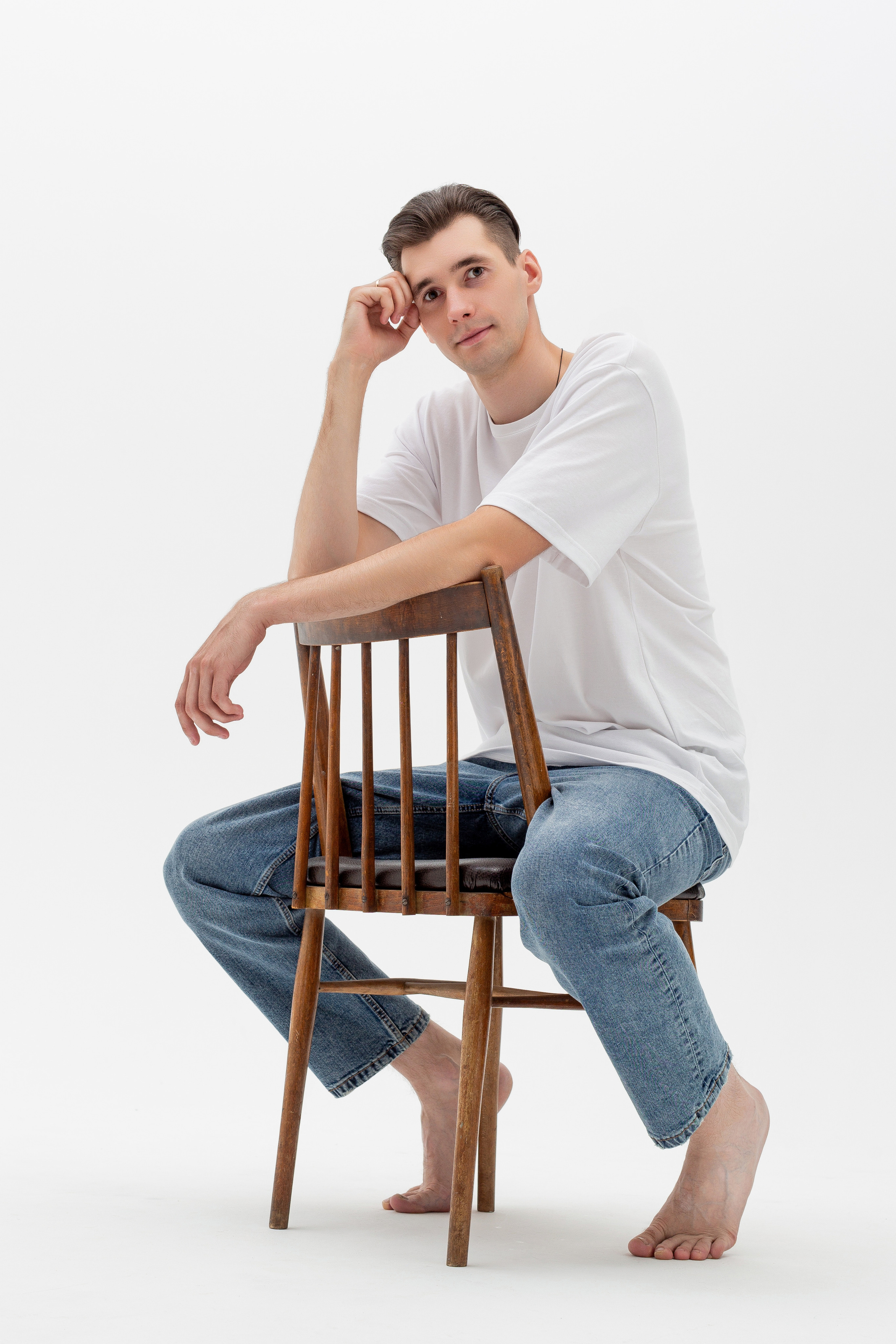 Студийный портрет мужчины сидящем на стуле, ростовой портрет, в белой футболке и джинсах на белом фоне