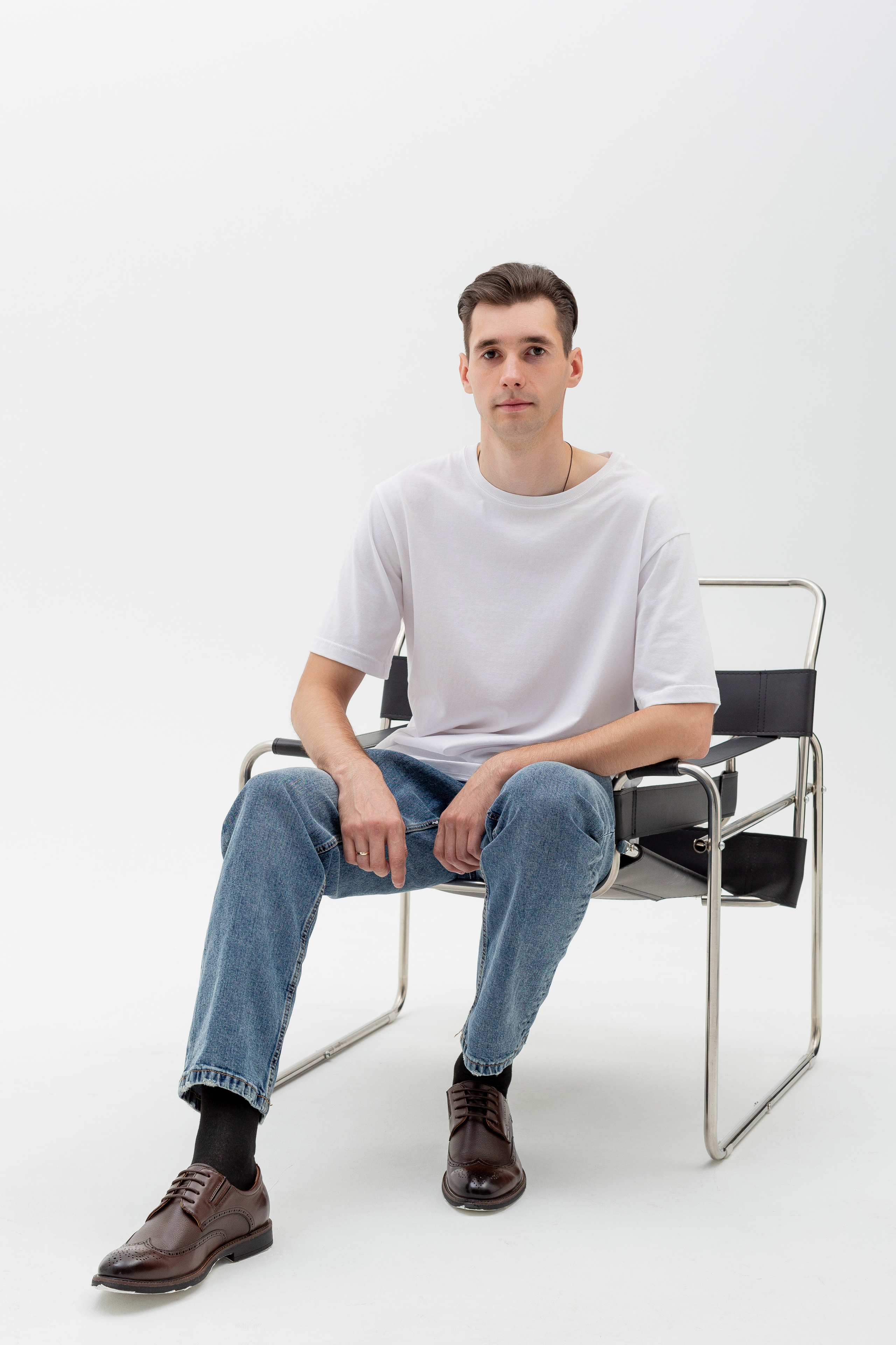 Студийный портрет мужчины сидящем на стуле, ростовой портрет, в белой футболке и джинсах на белом фоне