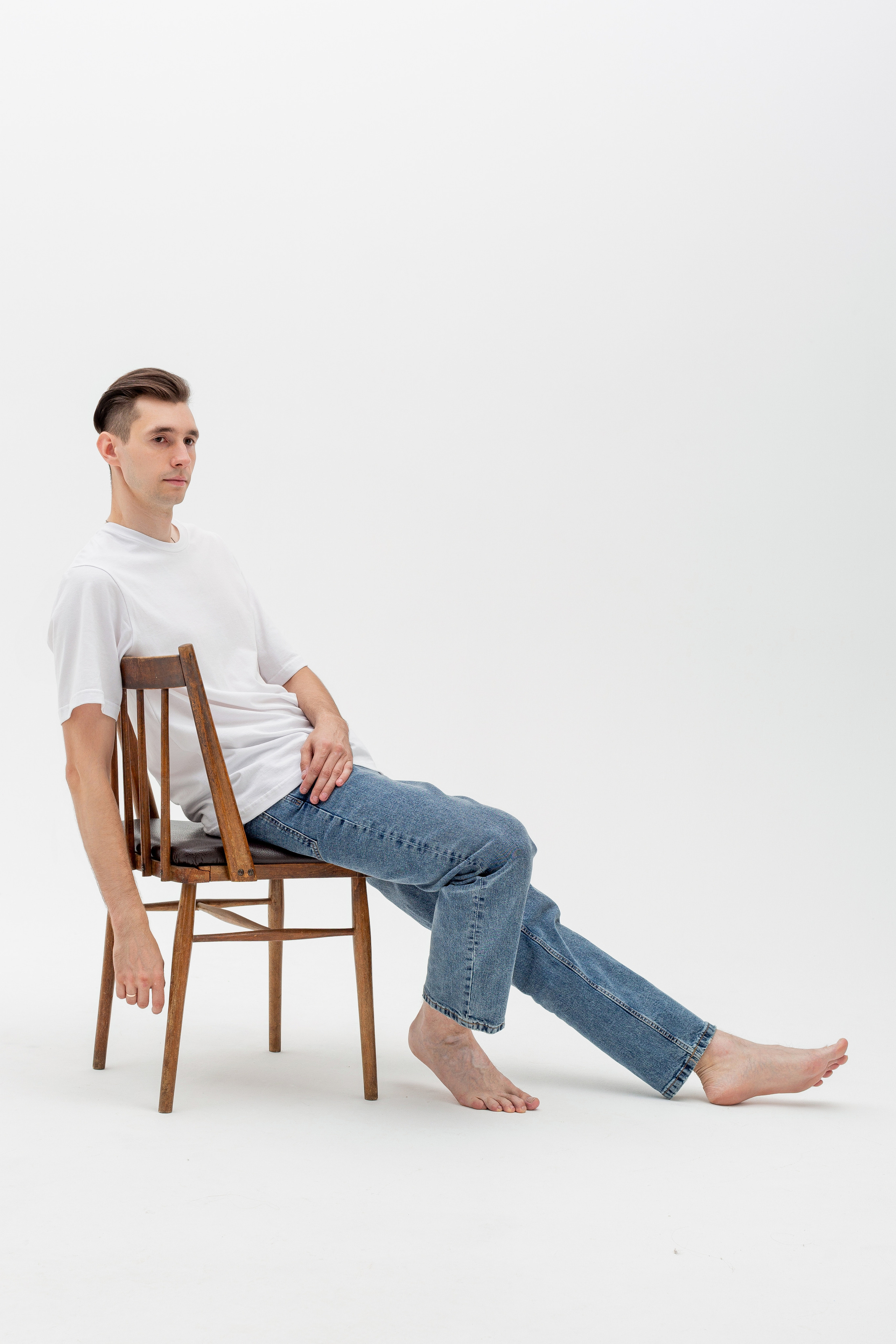 Студийный портрет мужчины сидящем на стуле, ростовой портрет, в белой футболке и джинсах на белом фоне