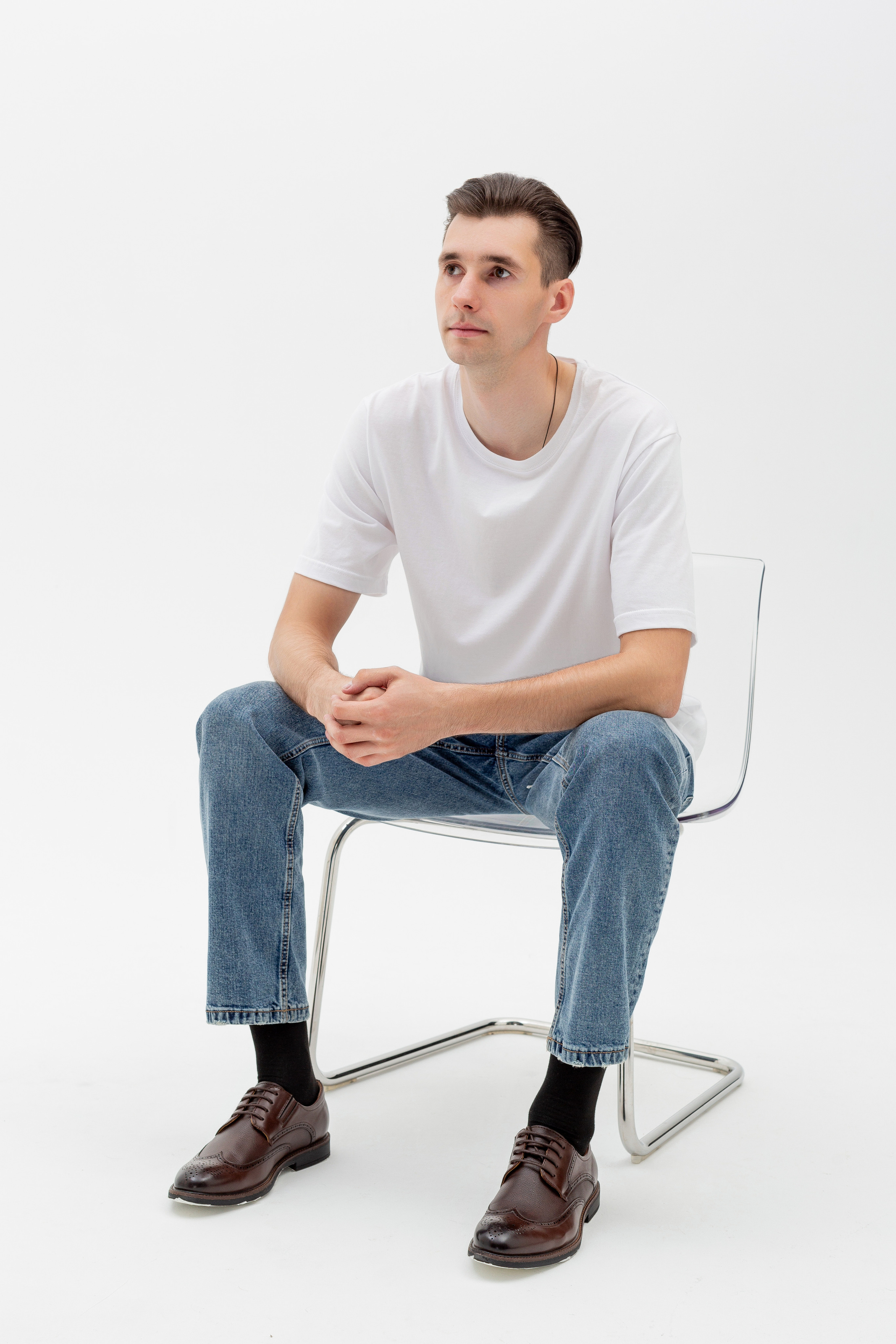 Студийный портрет мужчины сидящем на стуле, ростовой портрет, в белой футболке и джинсах на белом фоне