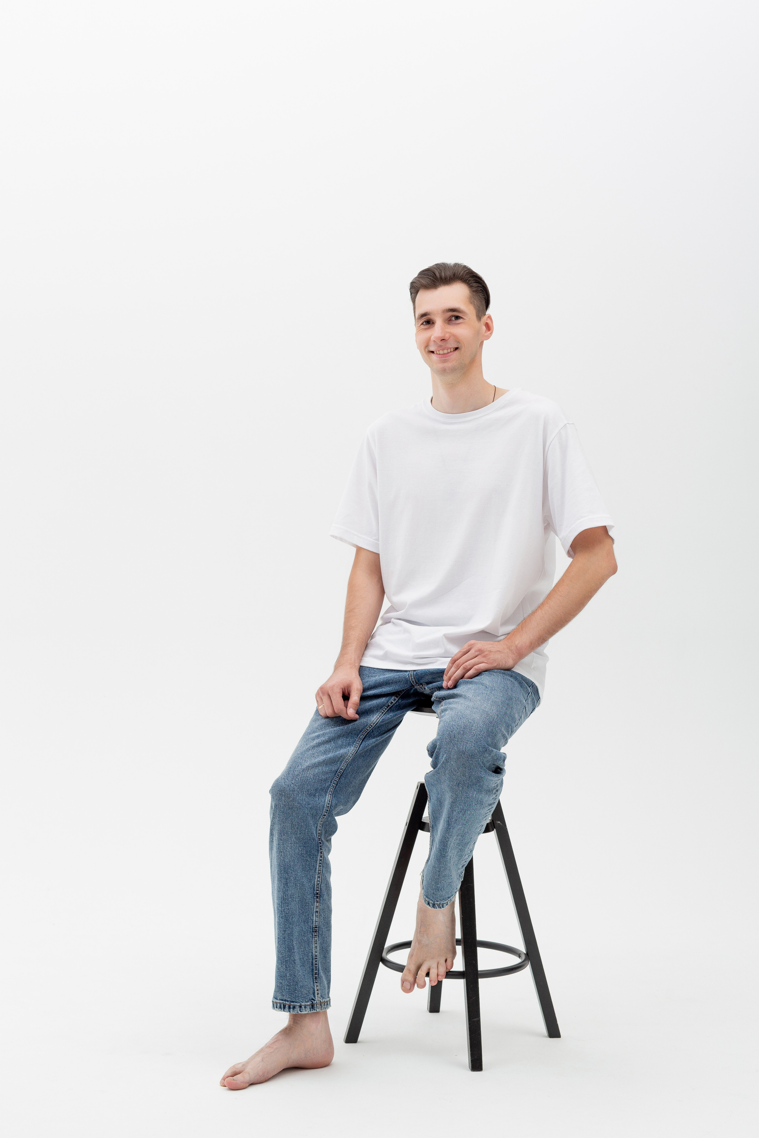 Студийный портрет мужчины сидящем на стуле, ростовой портрет, в белой футболке и джинсах на белом фоне