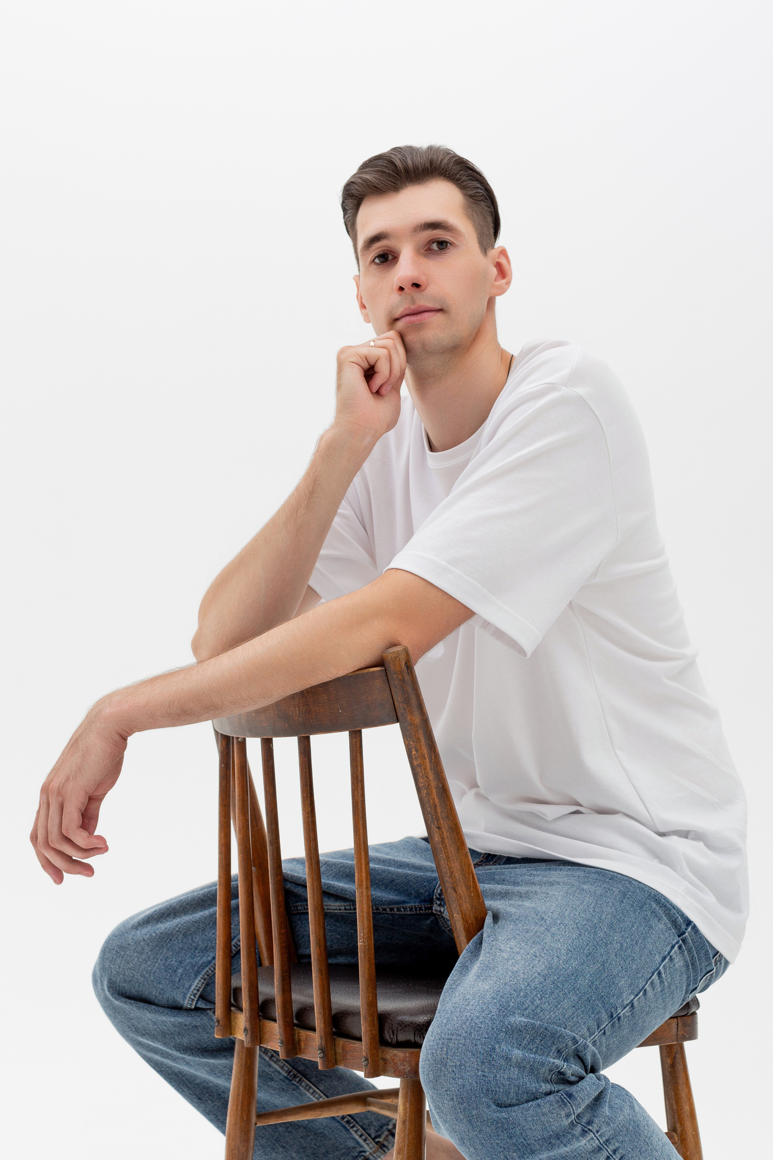 Студийный портрет мужчины сидящем на стуле, портрет 2/3, в белой футболке и джинсах на белом фоне