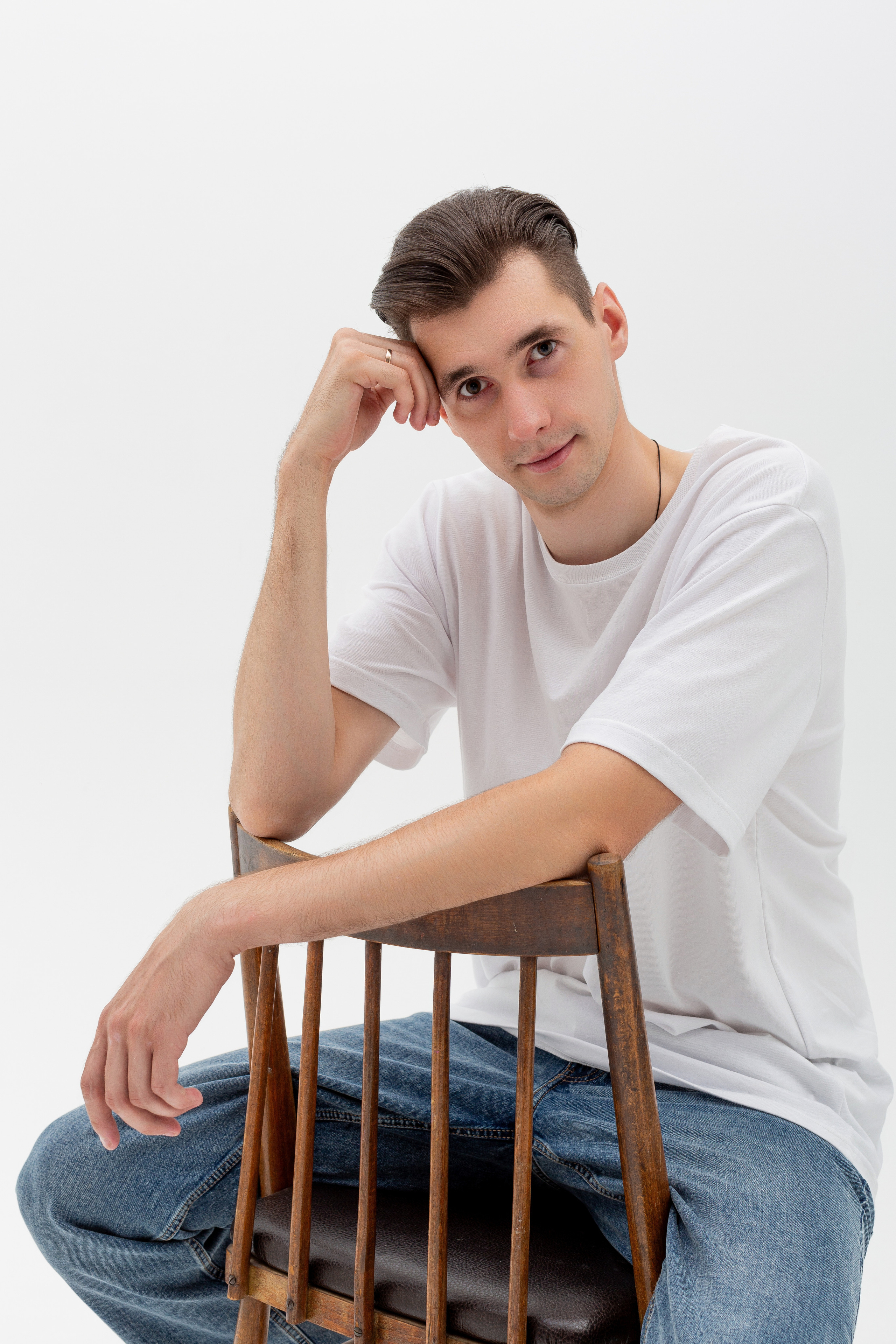 Студийный портрет мужчины сидящем на стуле, портрет 2/3, в белой футболке и джинсах на белом фоне