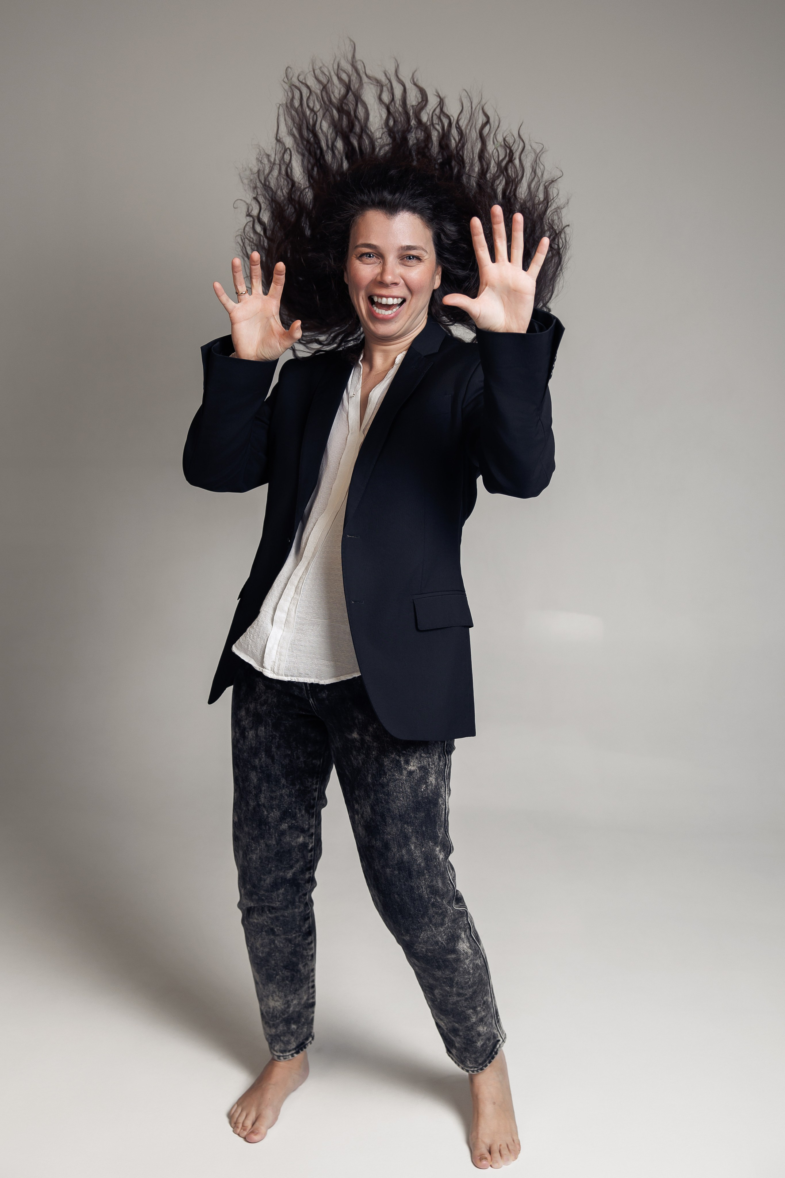 Женщина босиком с распущенными волосами улыбается и поднимает руки вверх, волосы в движении — кадр с живыми эмоциями.