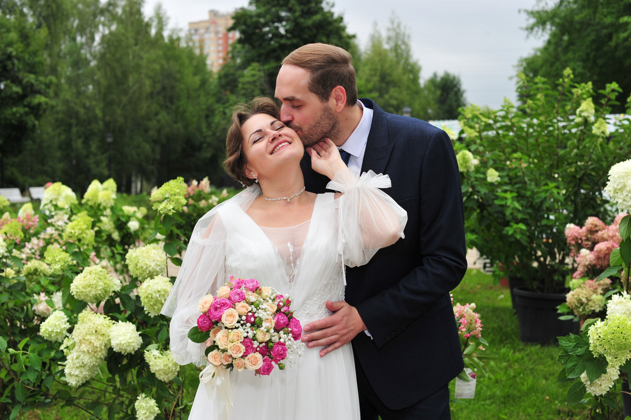 Свадьба в Царицыно пасмурным летним днем, поцелуй новобрачных на фоне цветущих гортензий 
