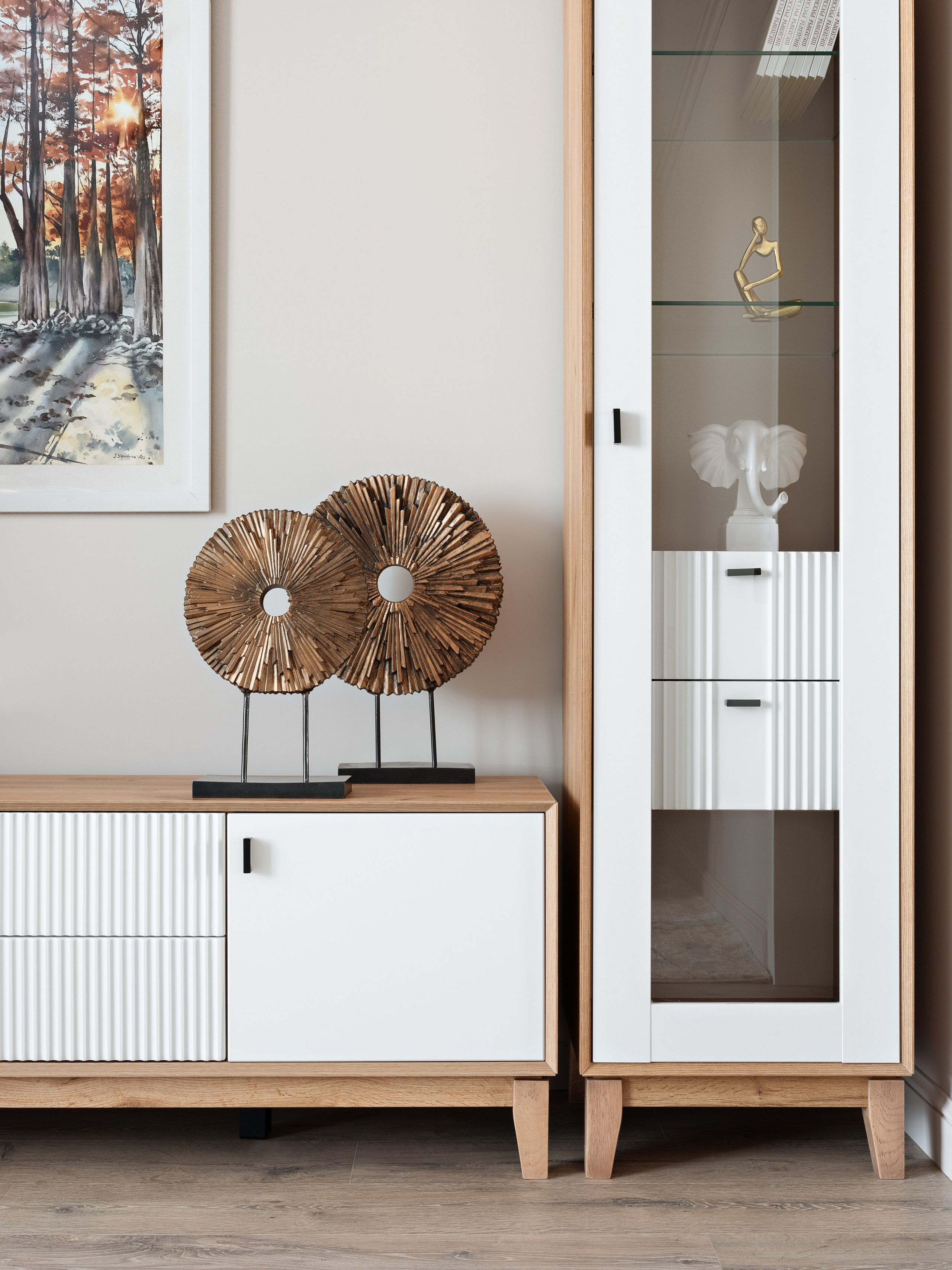 Современный интерьер гостиной с белым комодом и витриной из дерева и стекла, декорированными скульптурой слона и золотой фигуркой. Уютный акцент создают деревянные круглые элементы. Дизайн: Наталья Бунеева, стилист: Наталья Якушева, фото: Сергей Денисенко.