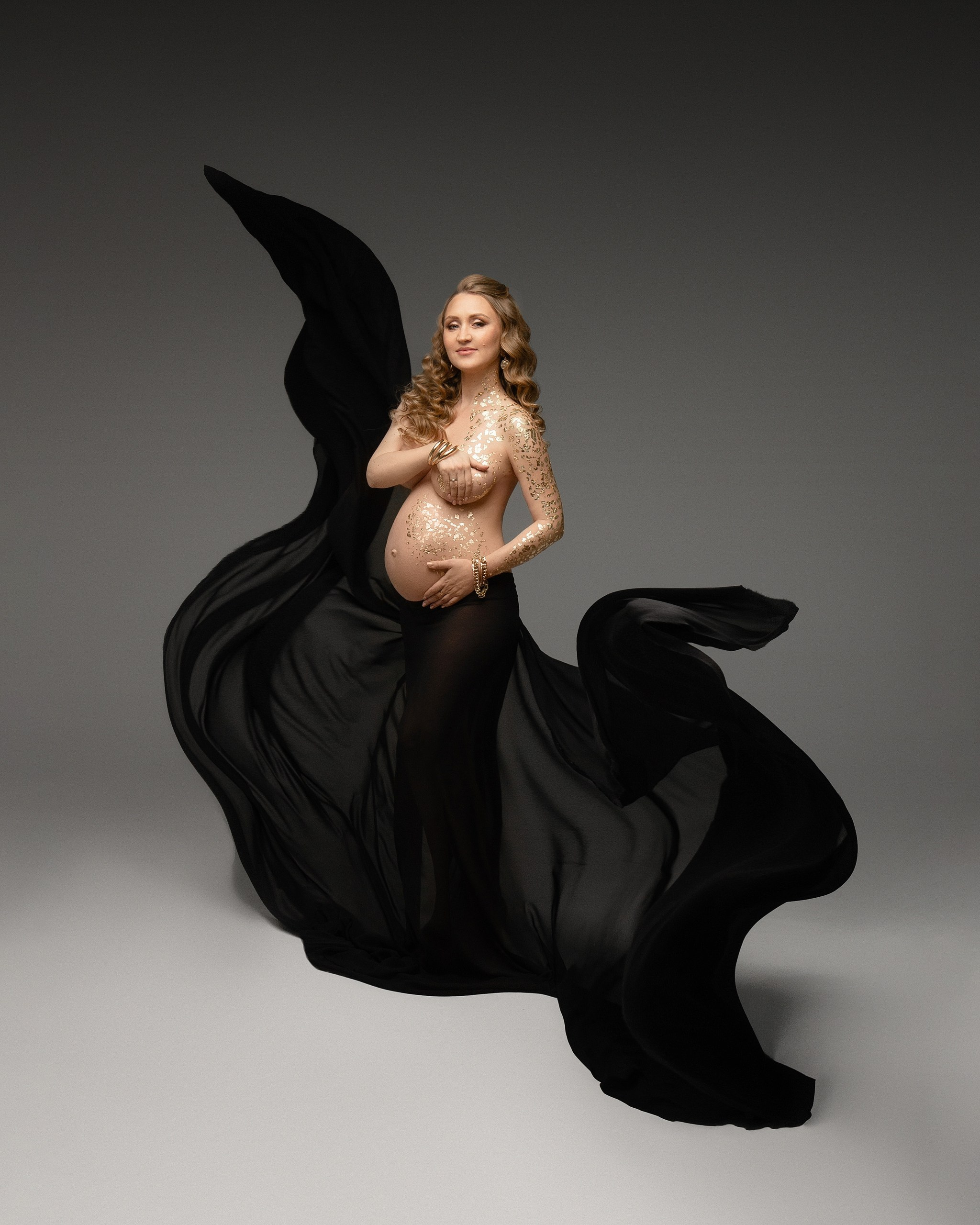 Беременная девушка в золотой потали и в летящей черной ткани