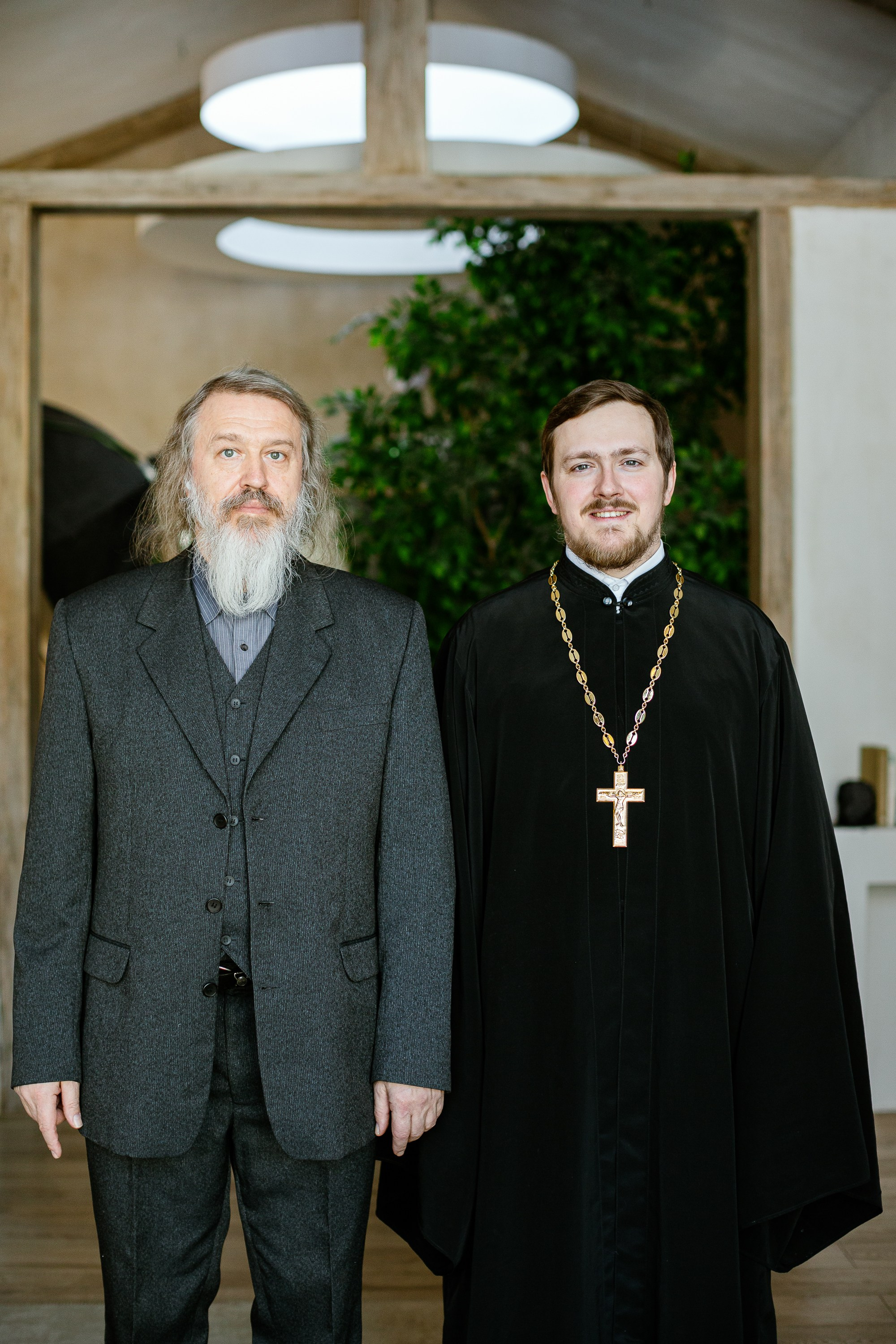 Отец священник с сыном священником стоят в фотостудии.