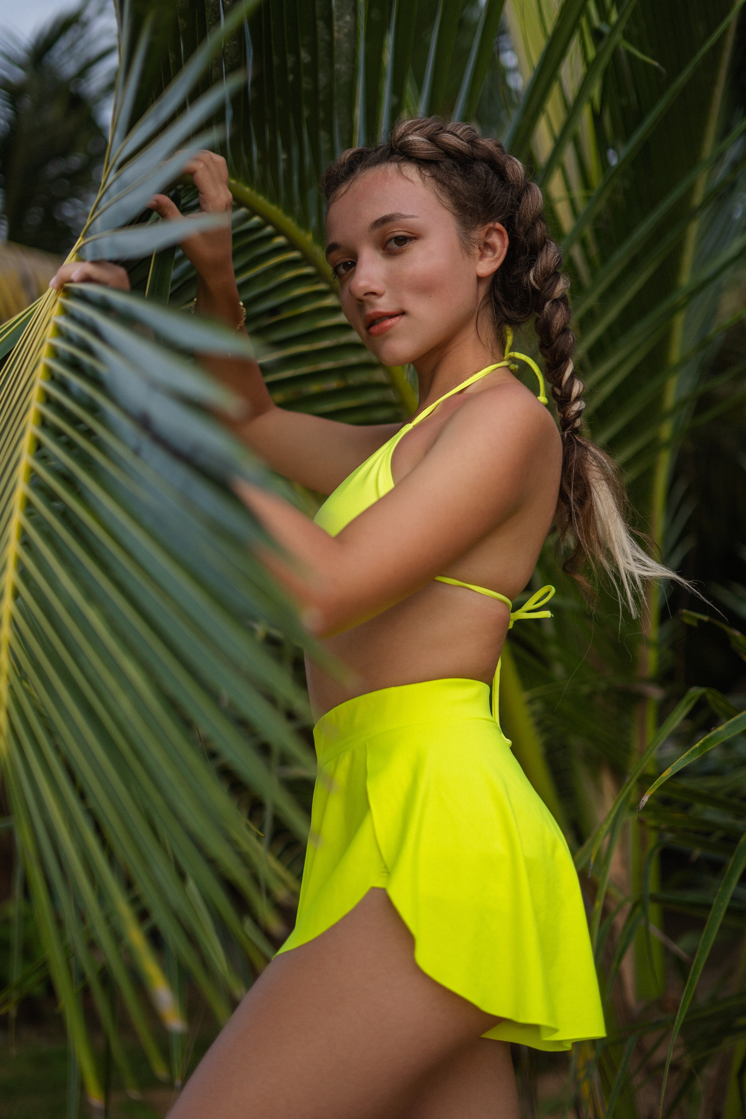 a girl with braids in a yellow swimsuit standing at the ocean's edge