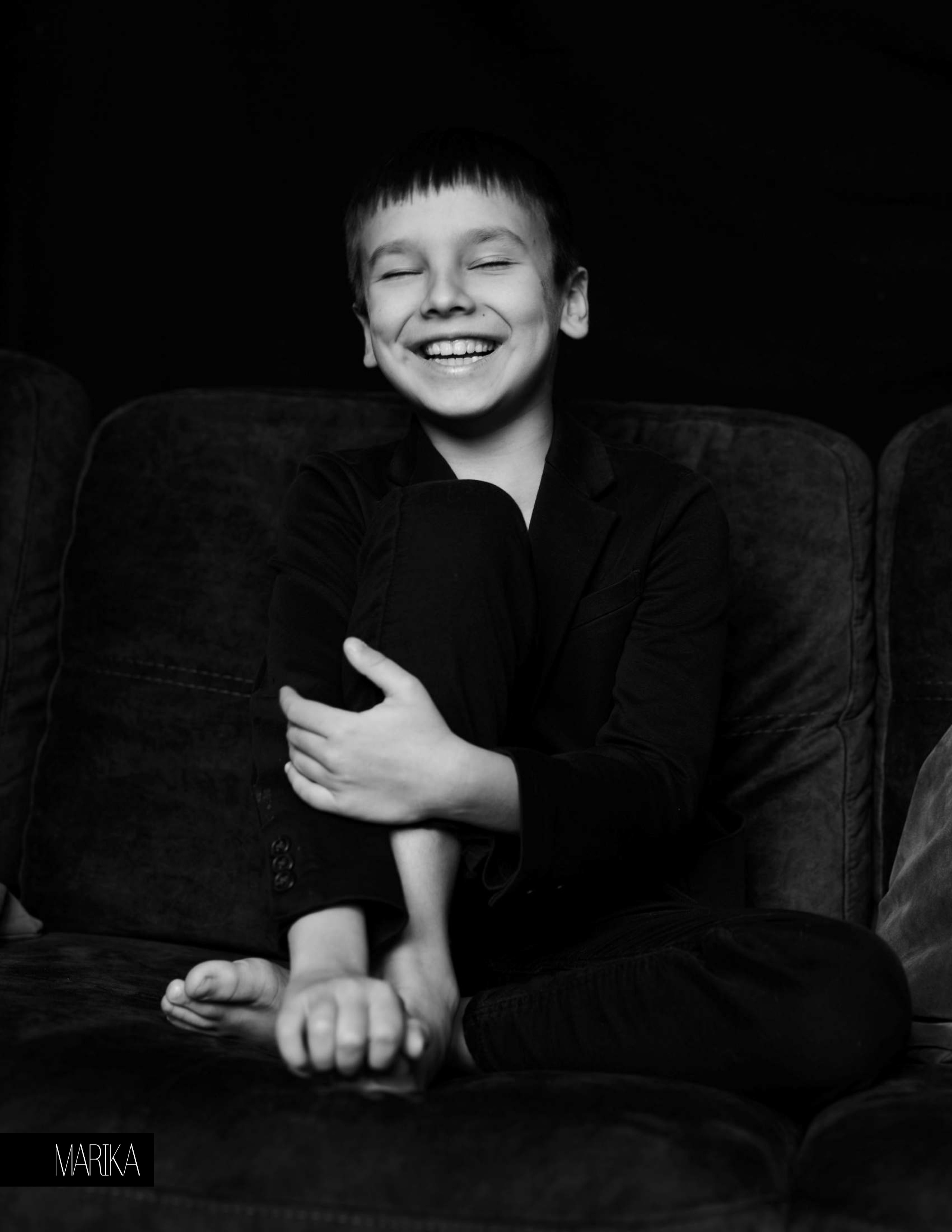 Детская черно-белая фотосессия в домашней студии. Ребенок сидит на диване и смеётся