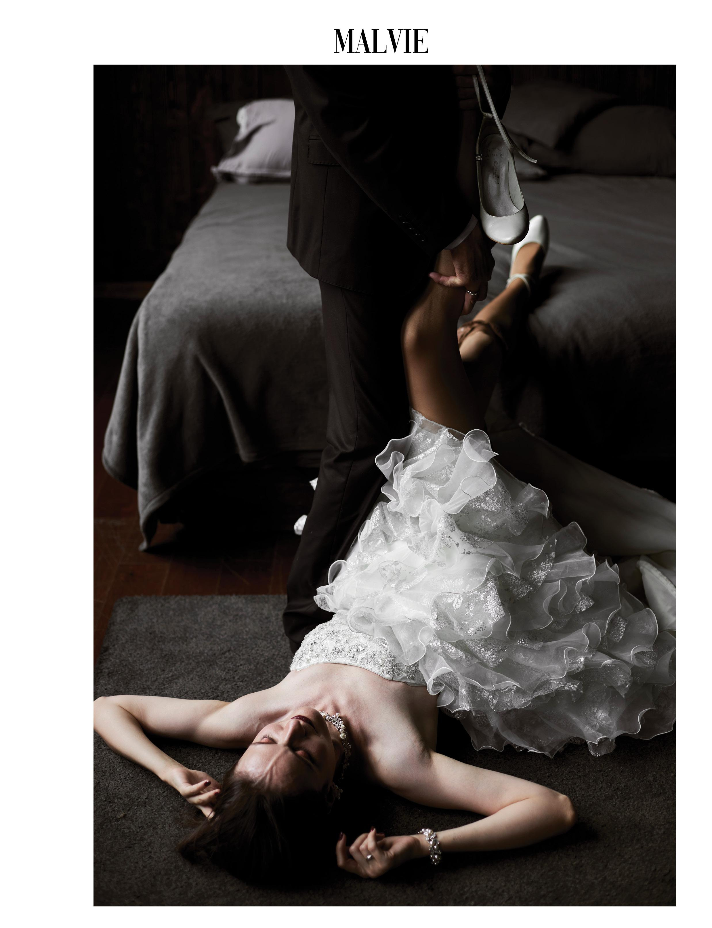 Невеста в свадебном платье лежит на полу, в то время как жених снимает чулок с её ноги