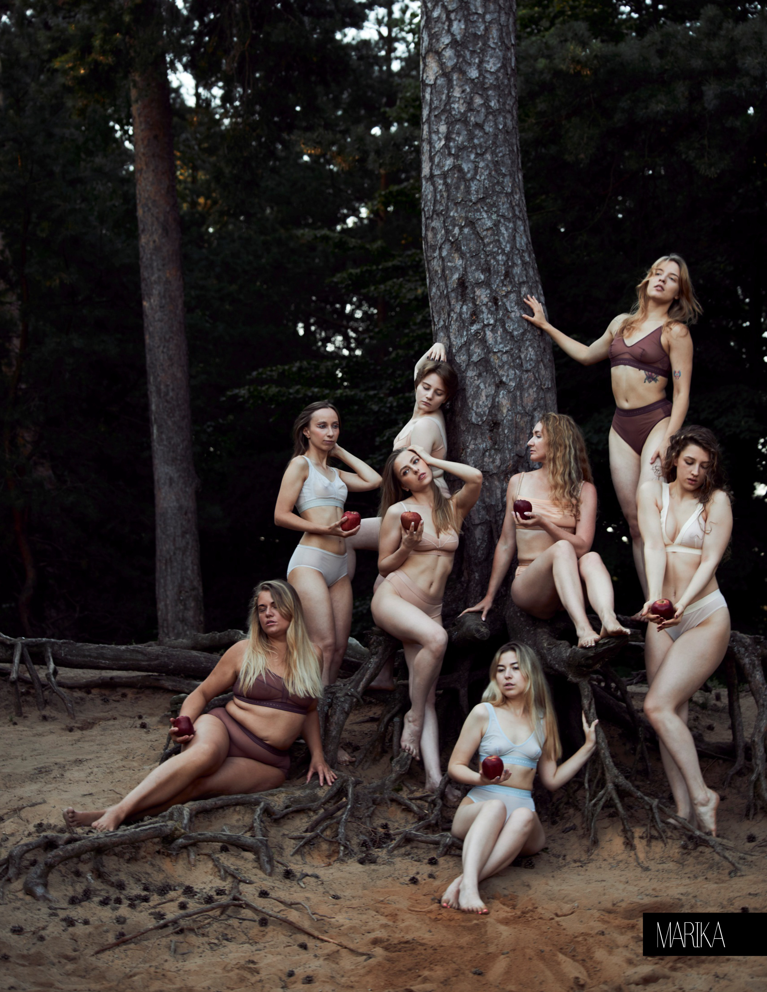 Несколько красивых  девушек в нижнем белье с красными яблоками в руках красиво расположились на колоритном дереве