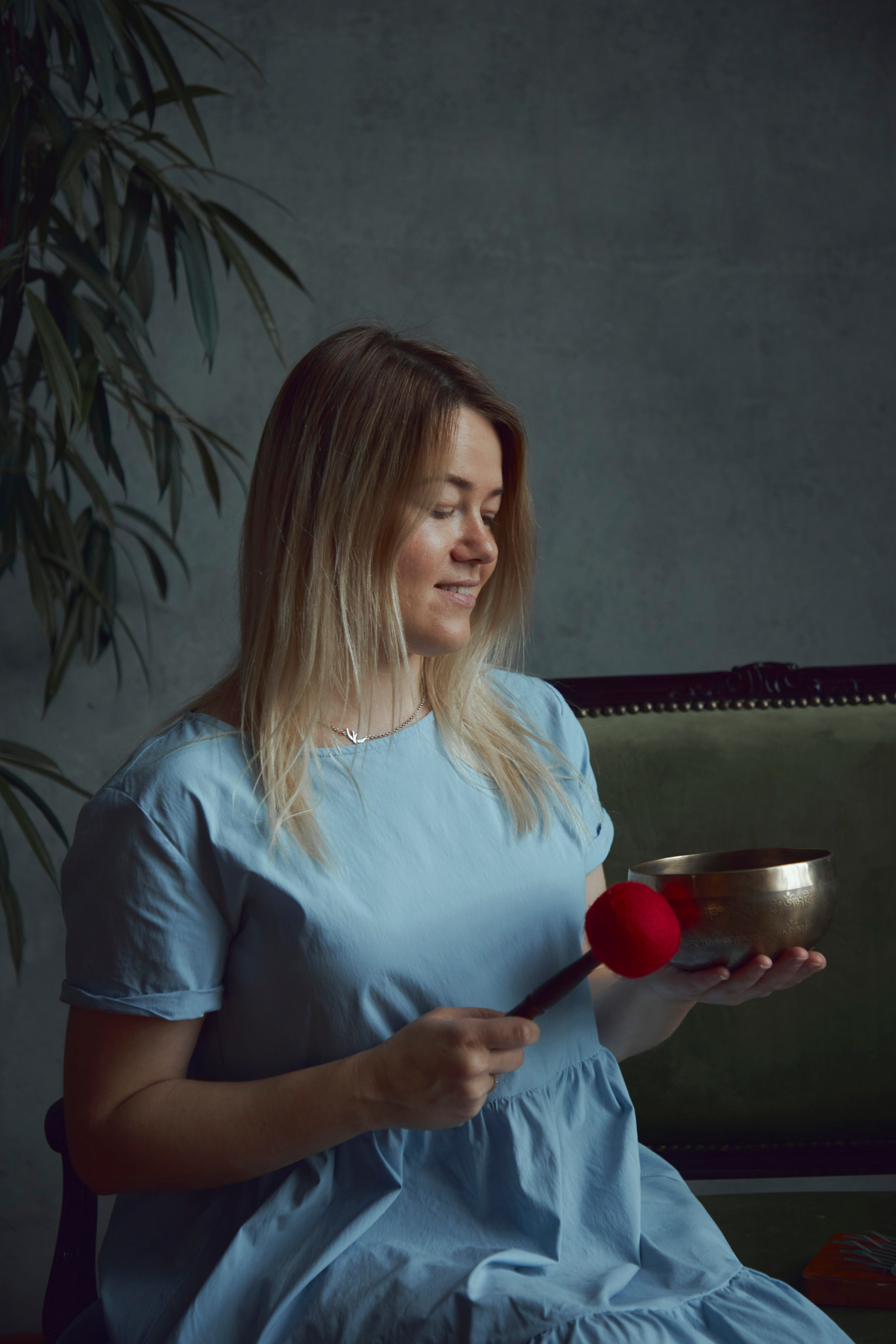 Девушка в синим платье сидит на софе с тибетской поющей чашей в руках
