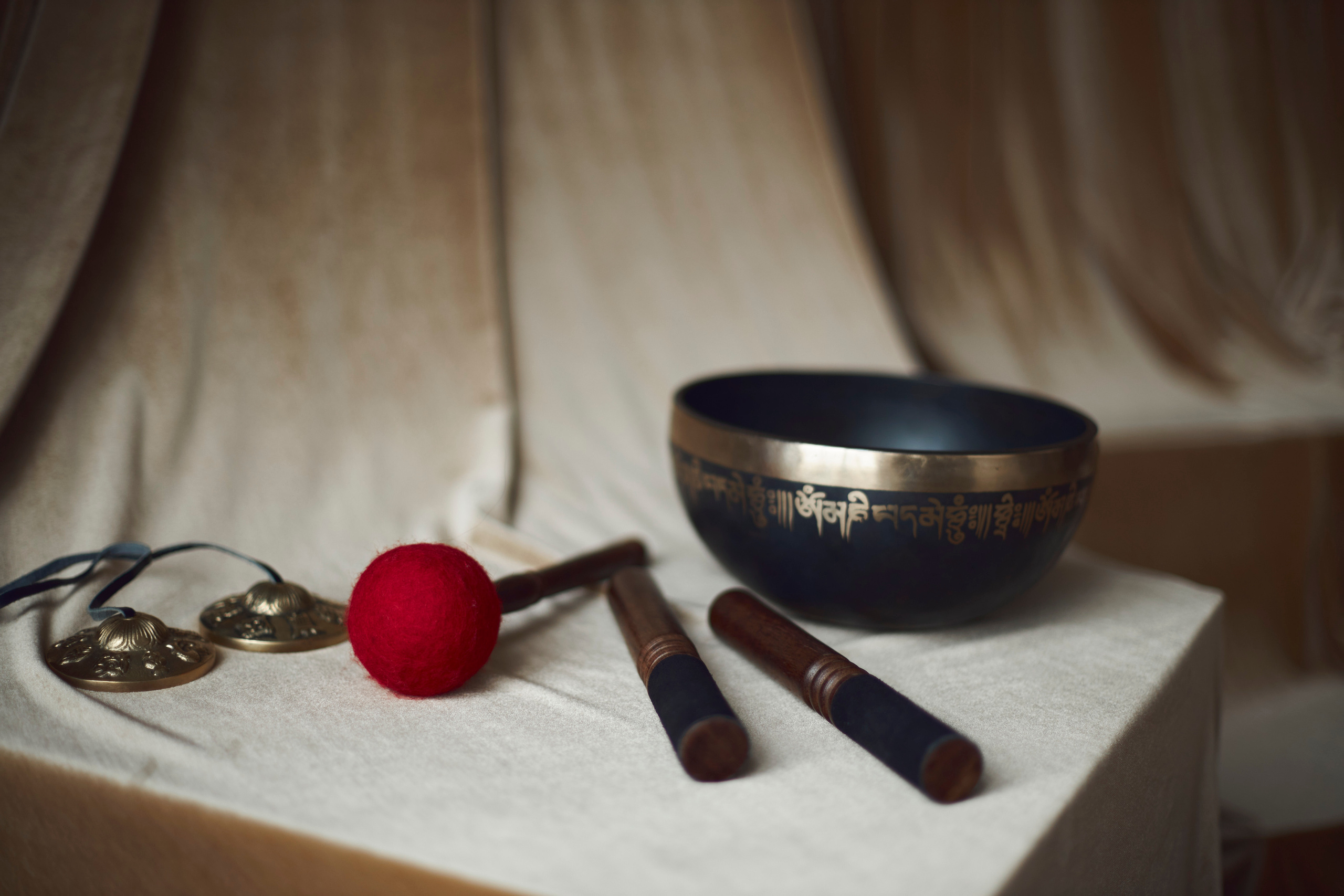 На бежевой ткани стоит тибетская поющая чаша и стики для извлечения звука