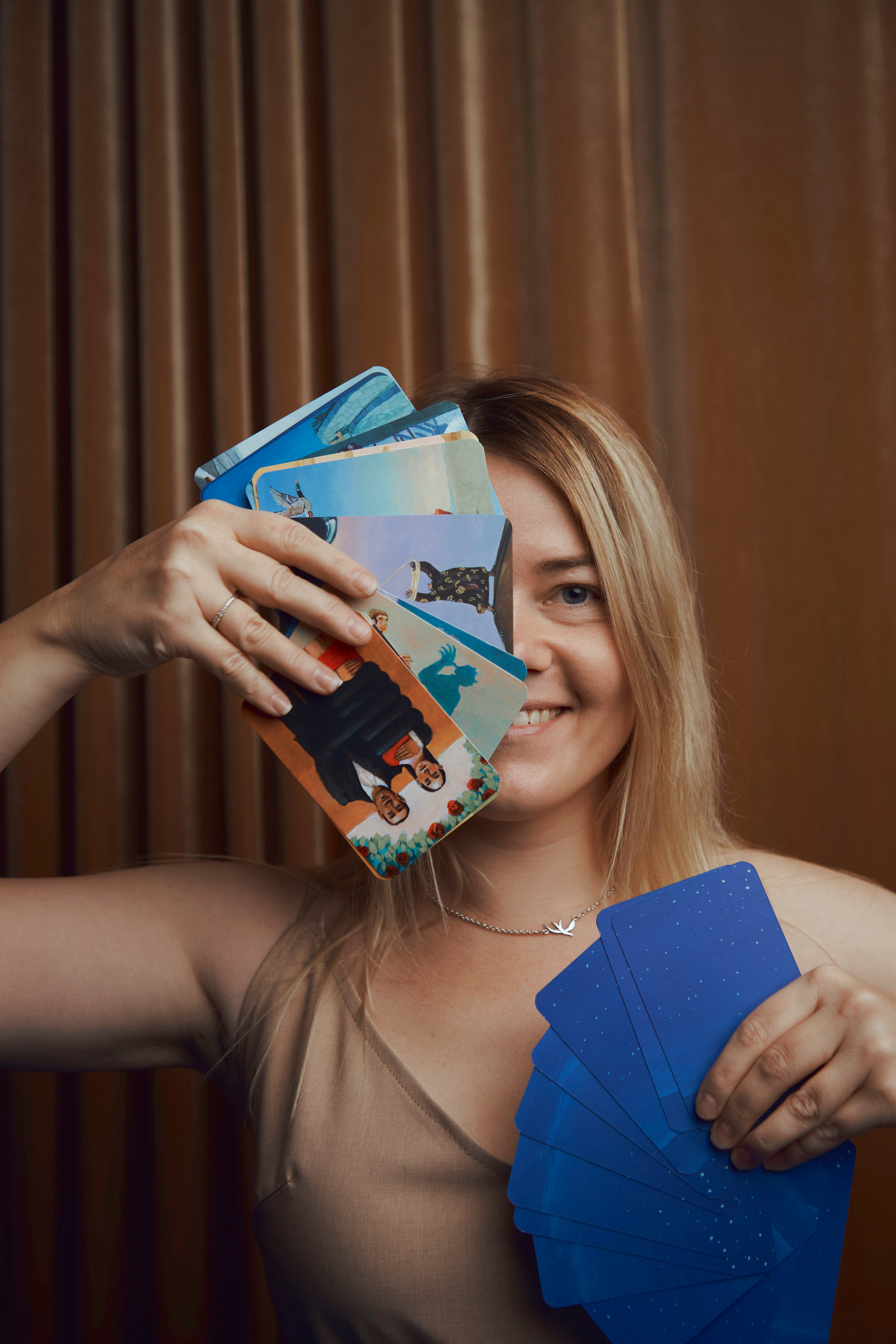 Девушка держит в руках карты Таро сложенные веером в обеих руках, частично закрывая ими своё лицо