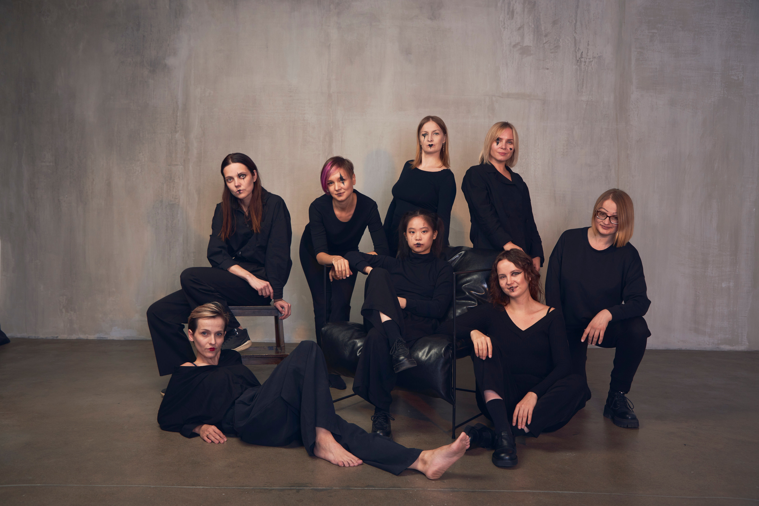 Компания из восьми человек в черных костюмах на фоне серой бетонной стены в студии