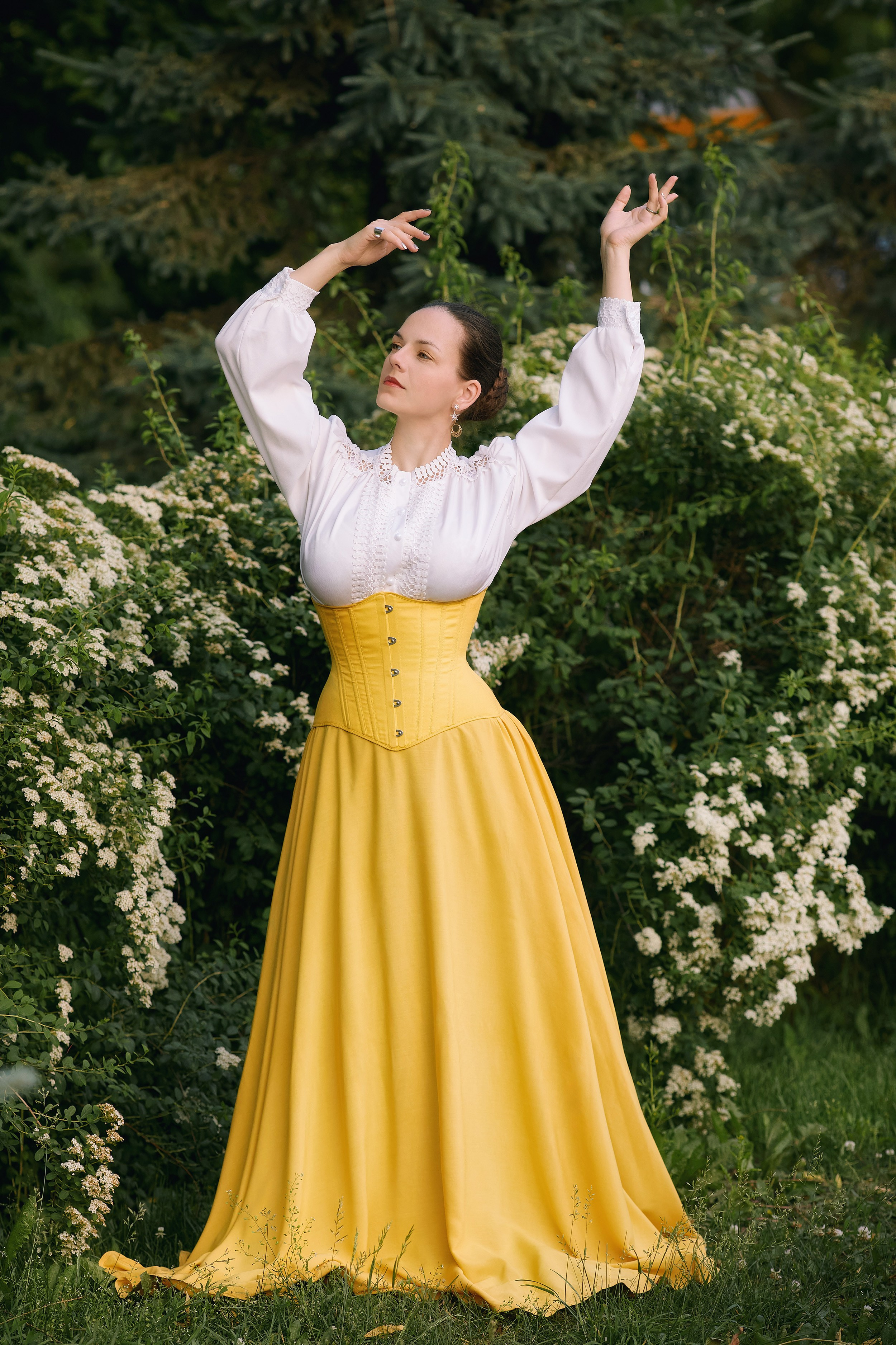 Атмосферная женская фотосъёмка в летнем саду в Находке. Модель в белой блузке и длинном жёлтом платье позирует на фоне белых цветов